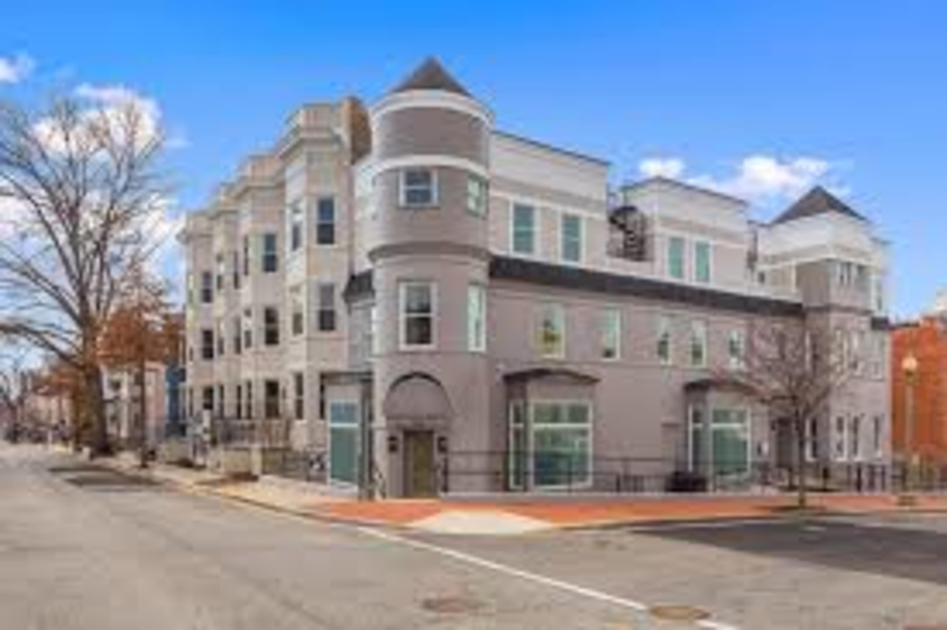 A modern, multi-unit building located at the corner of a street, featuring a mix of brick and stucco exteriors.