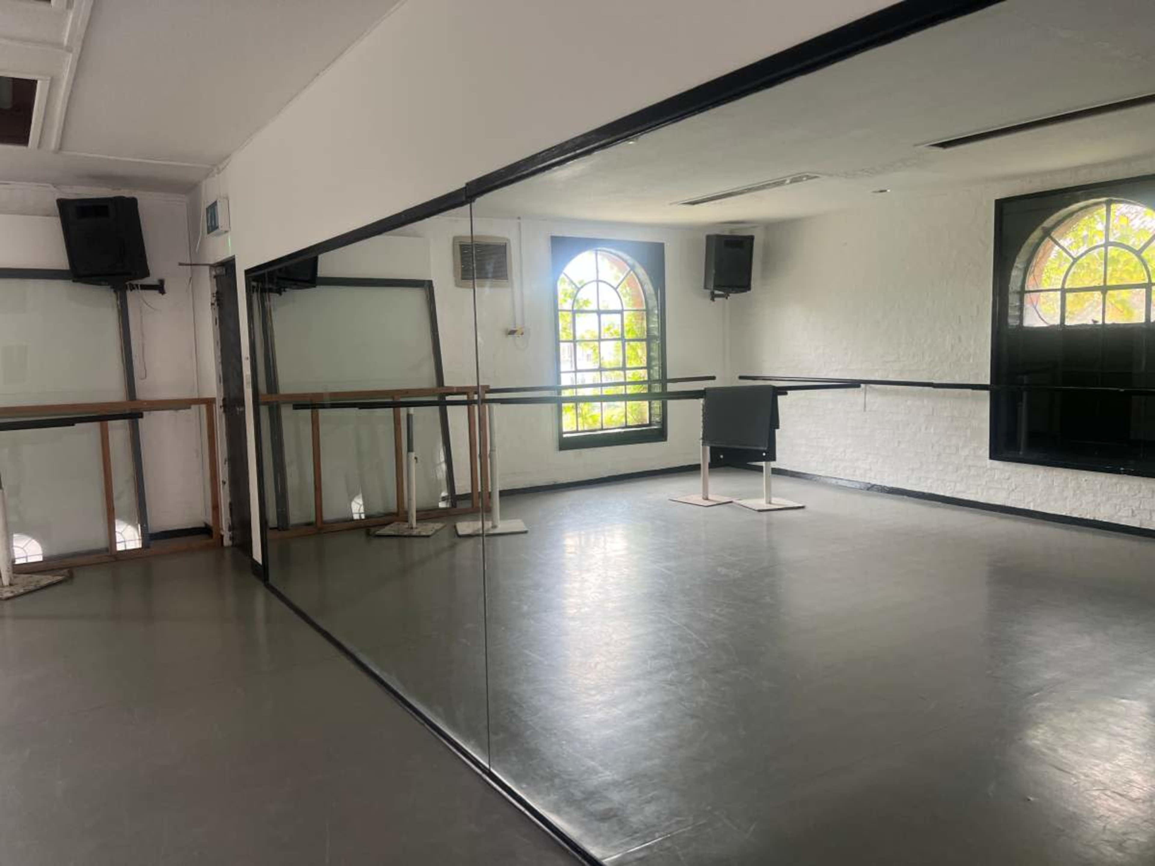 The image shows a dance studio with mirrored walls, wooden ballet bars, and a window providing natural light.