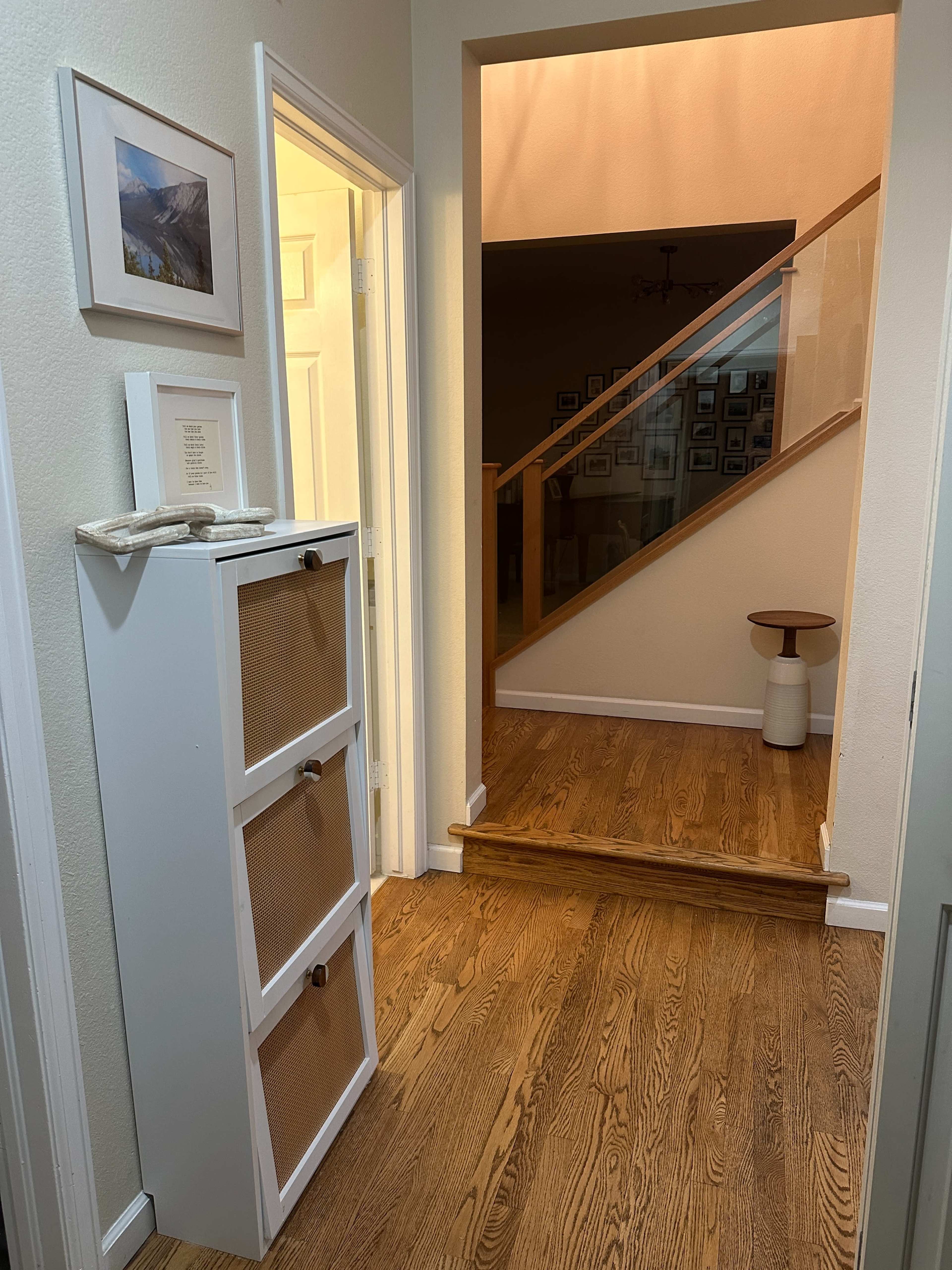 A hallway features a white cabinet with three drawers, leading to a staircase illuminated by warm light.