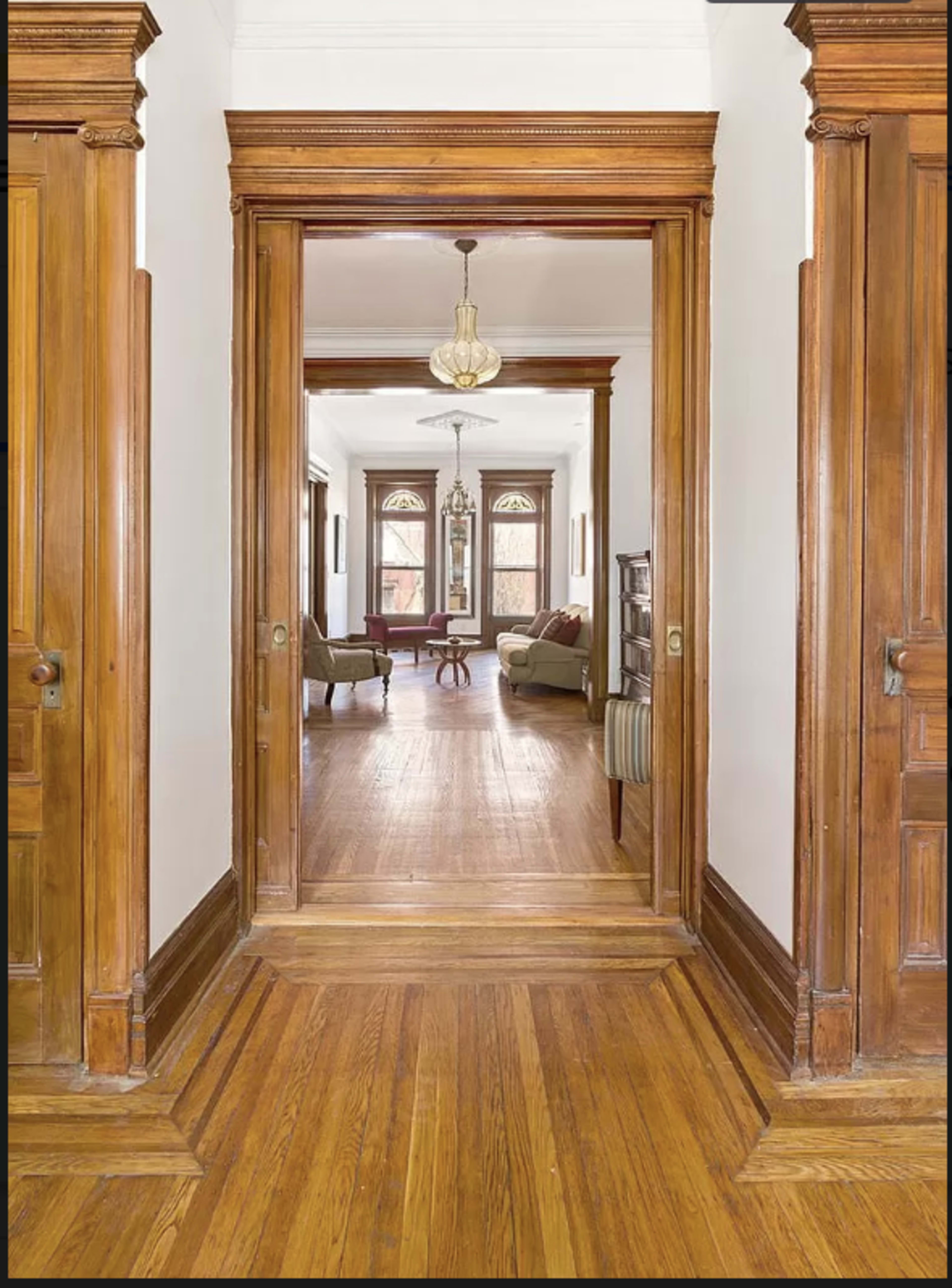The image shows a hallway with wooden door frames leading to a living room furnished with a couch and a table.