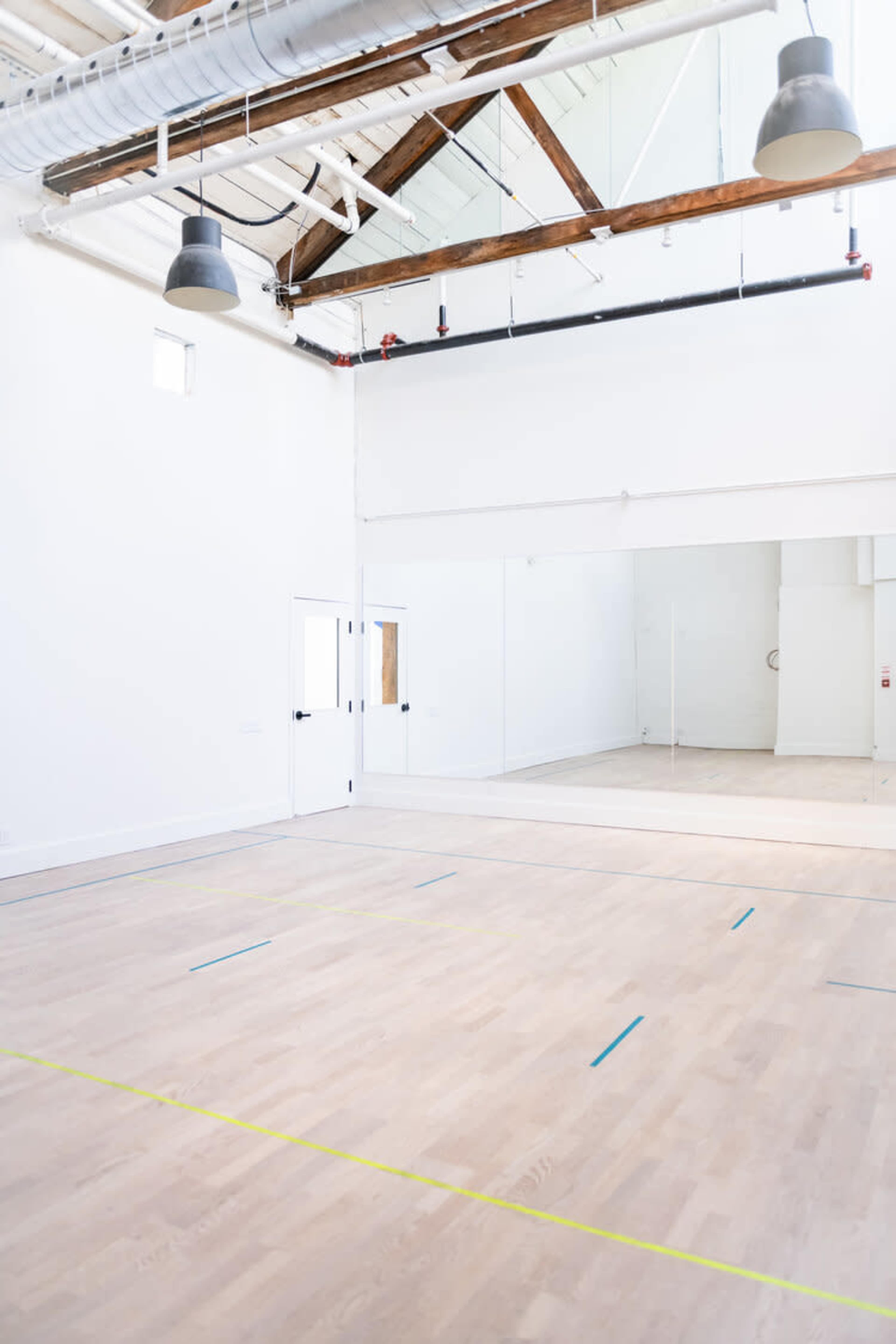 A spacious, empty studio with light wooden flooring and large mirrors along one wall.