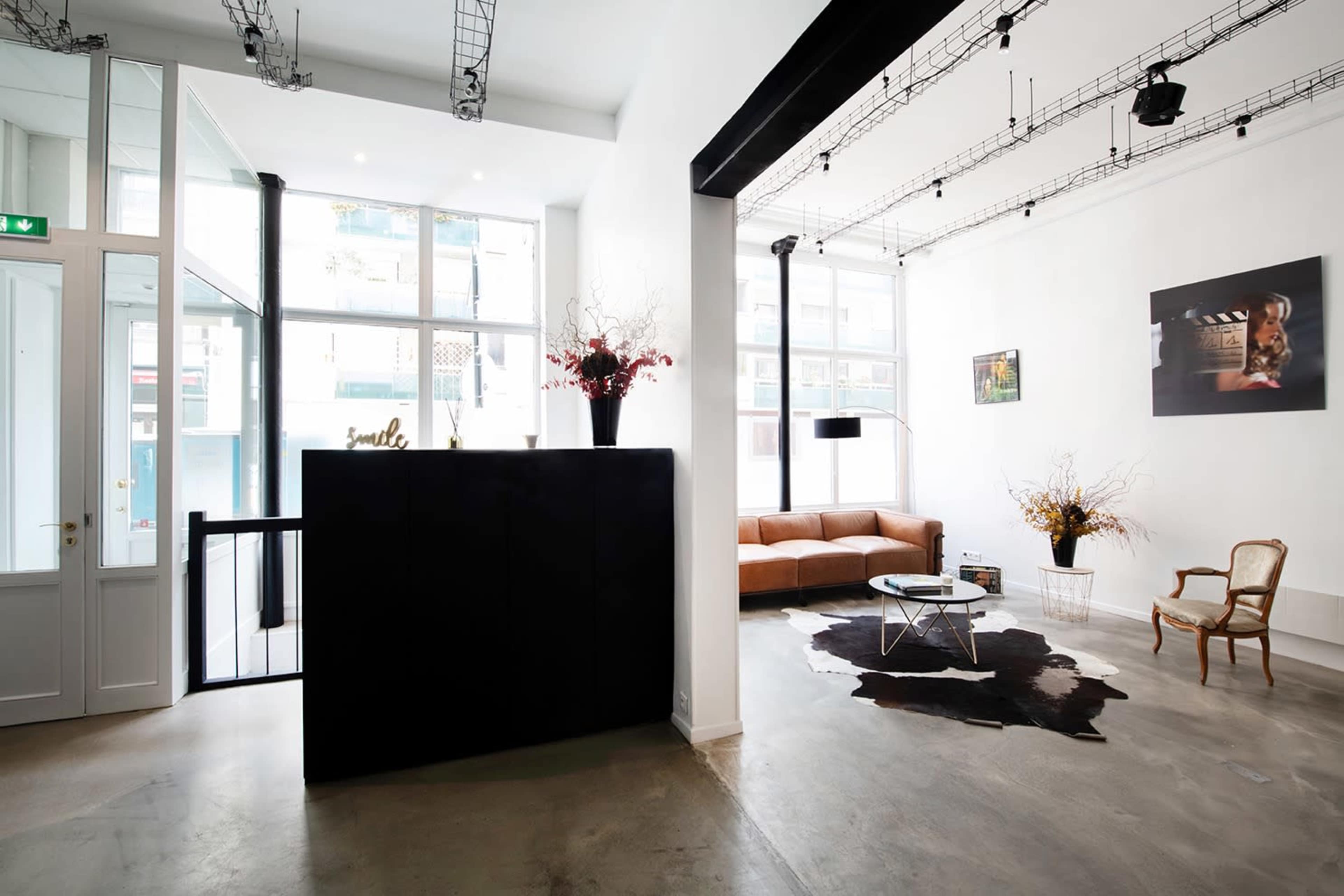 A modern interior space with a brown leather sofa, a round coffee table on a cowhide rug, and large windows allowing natural light to enter.