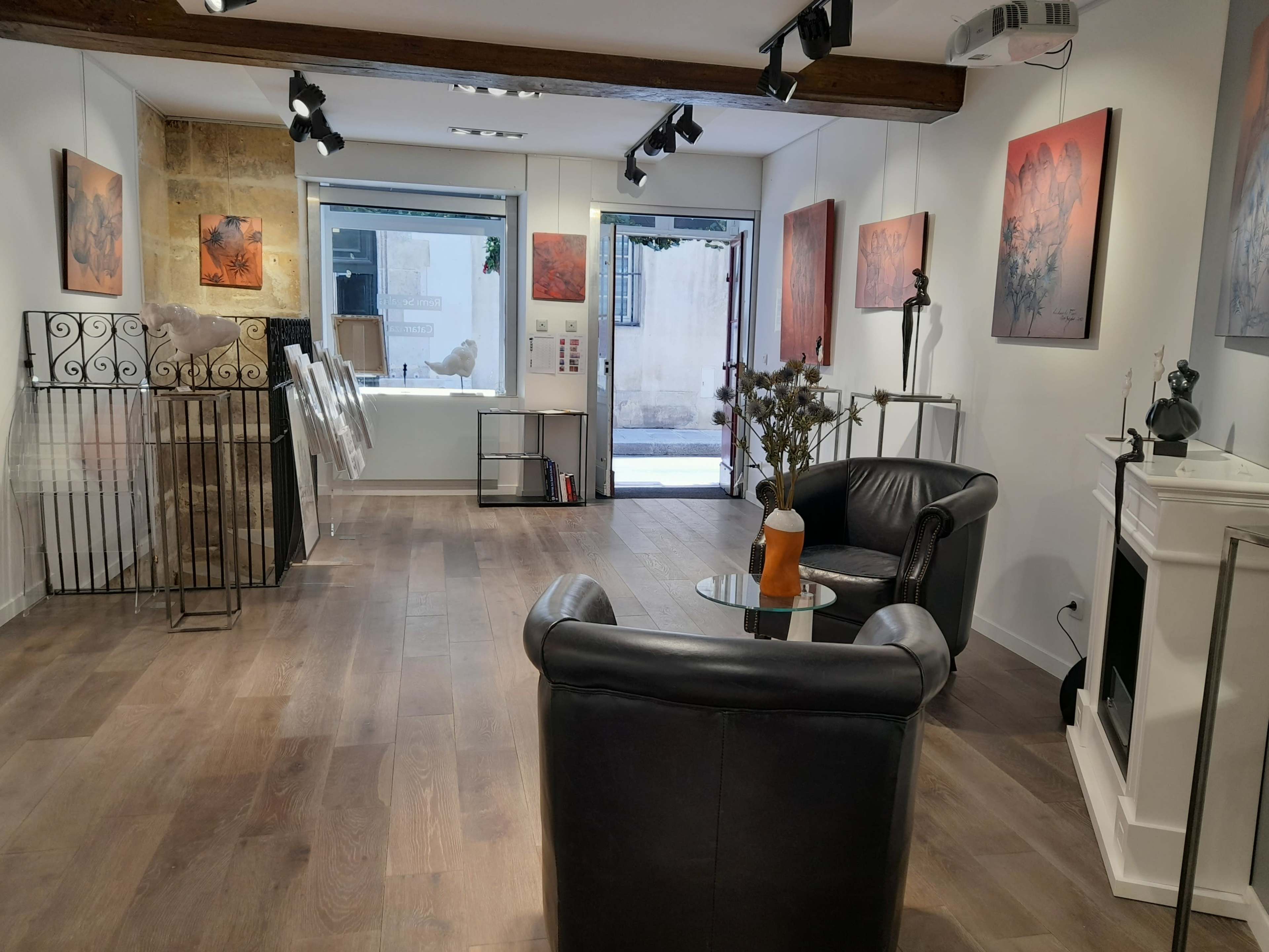 An art gallery featuring several artworks displayed on the walls, with black leather chairs and a coffee table in the center of the room.