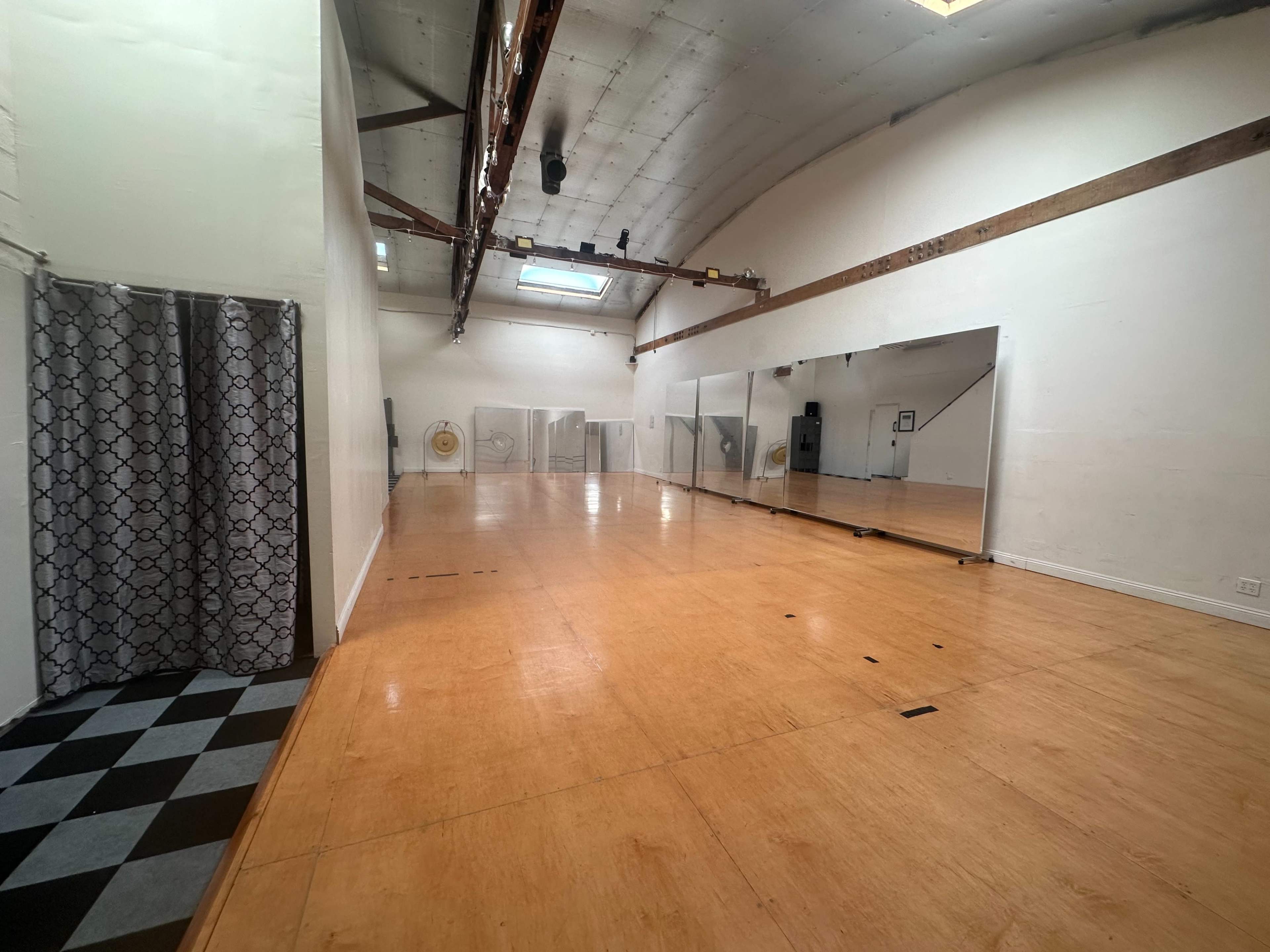 The image shows a spacious dance studio with a polished wooden floor, large mirrors on one wall, and a patterned black-and-white tile section in one corner.