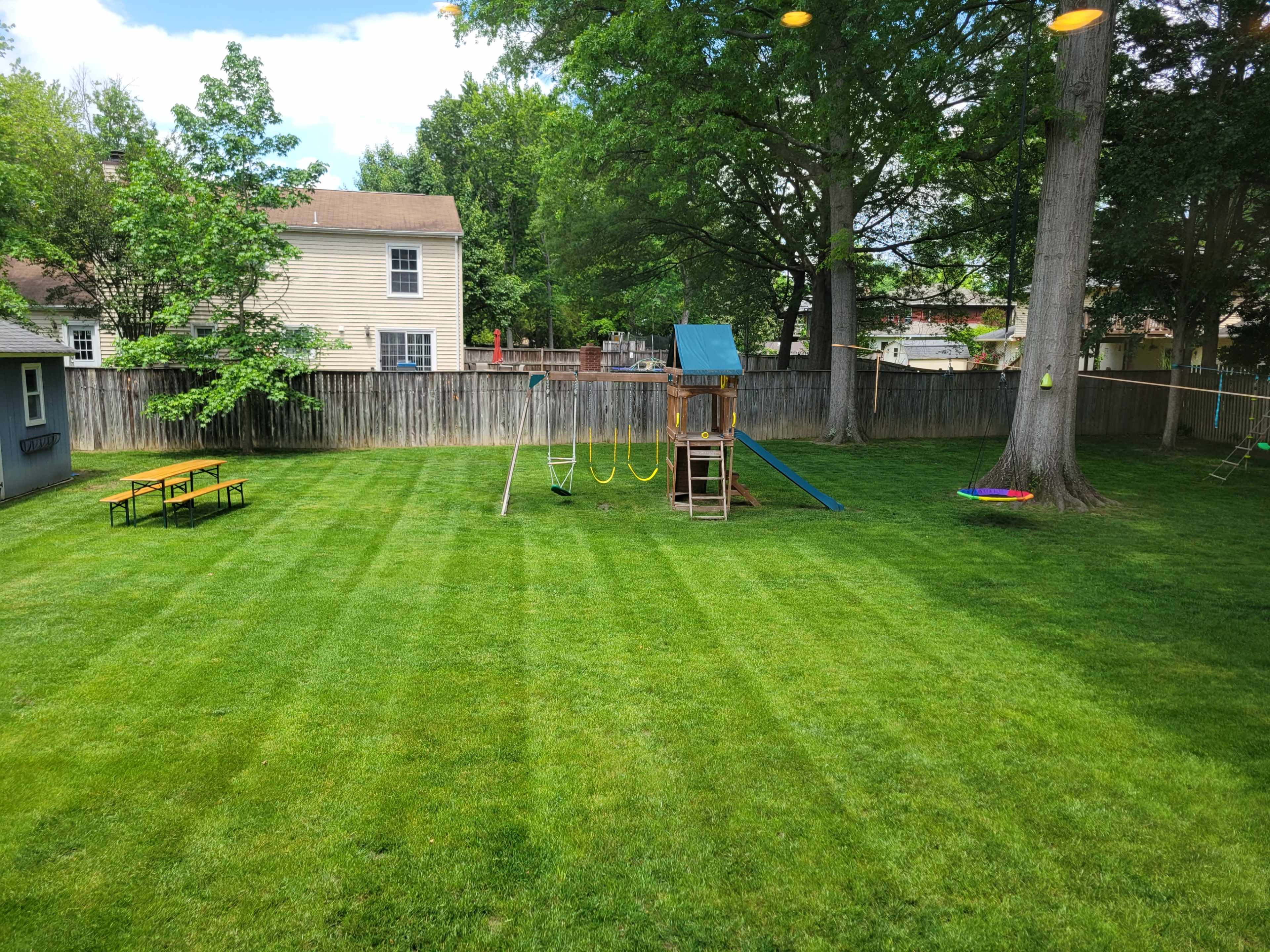 The image shows a neatly maintained backyard with a playground set, picnic table, and well-manicured grass.