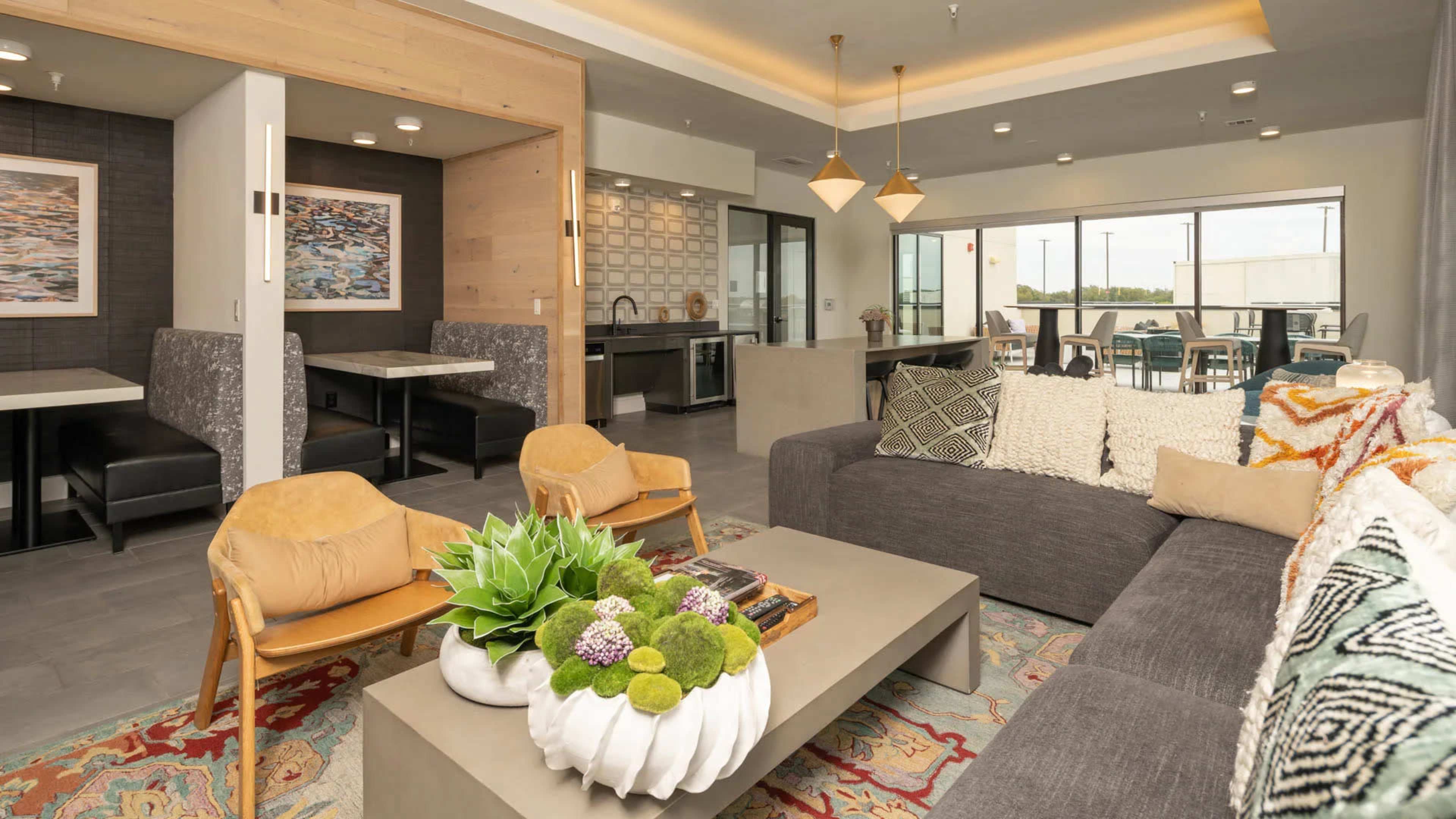 The image shows a modern living space featuring a gray sofa, wooden chairs, a decorative coffee table with greenery, and dining areas in the background.