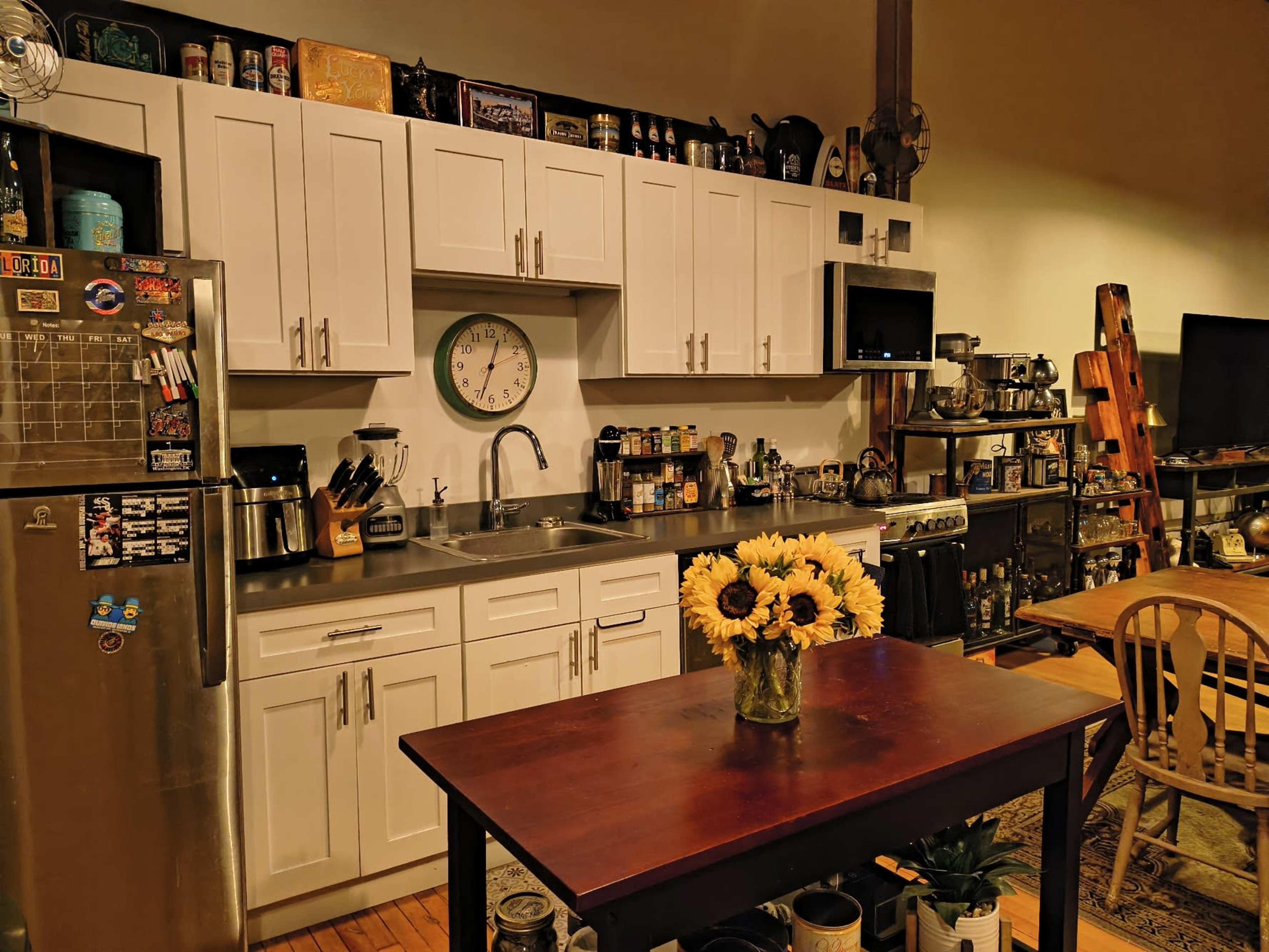 The kitchen features white cabinetry, stainless steel appliances, and a wooden table with a vase of sunflowers in the center.