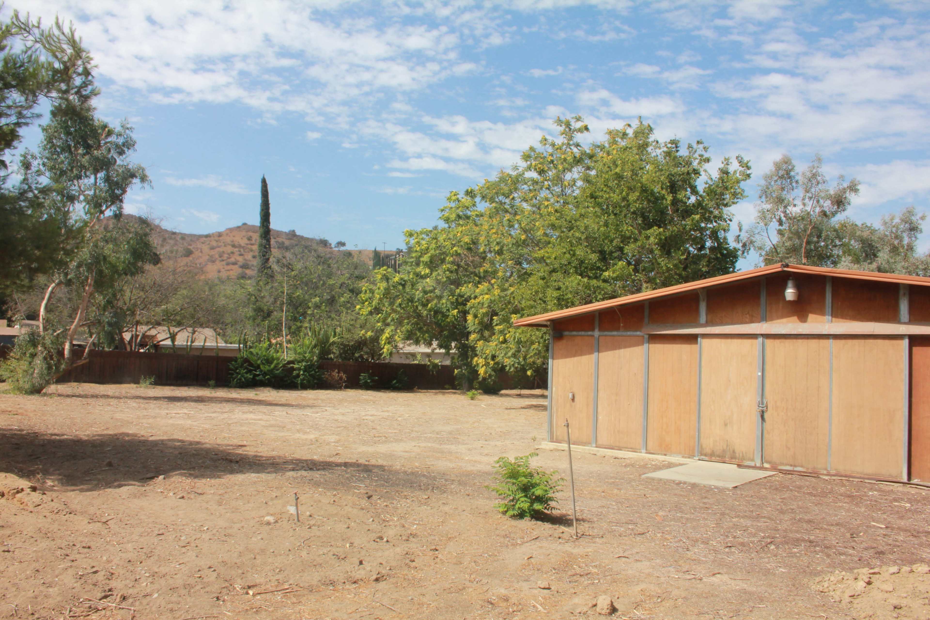 A bare, dry landscape with a wooden shed and sparse vegetation under a partly cloudy sky.