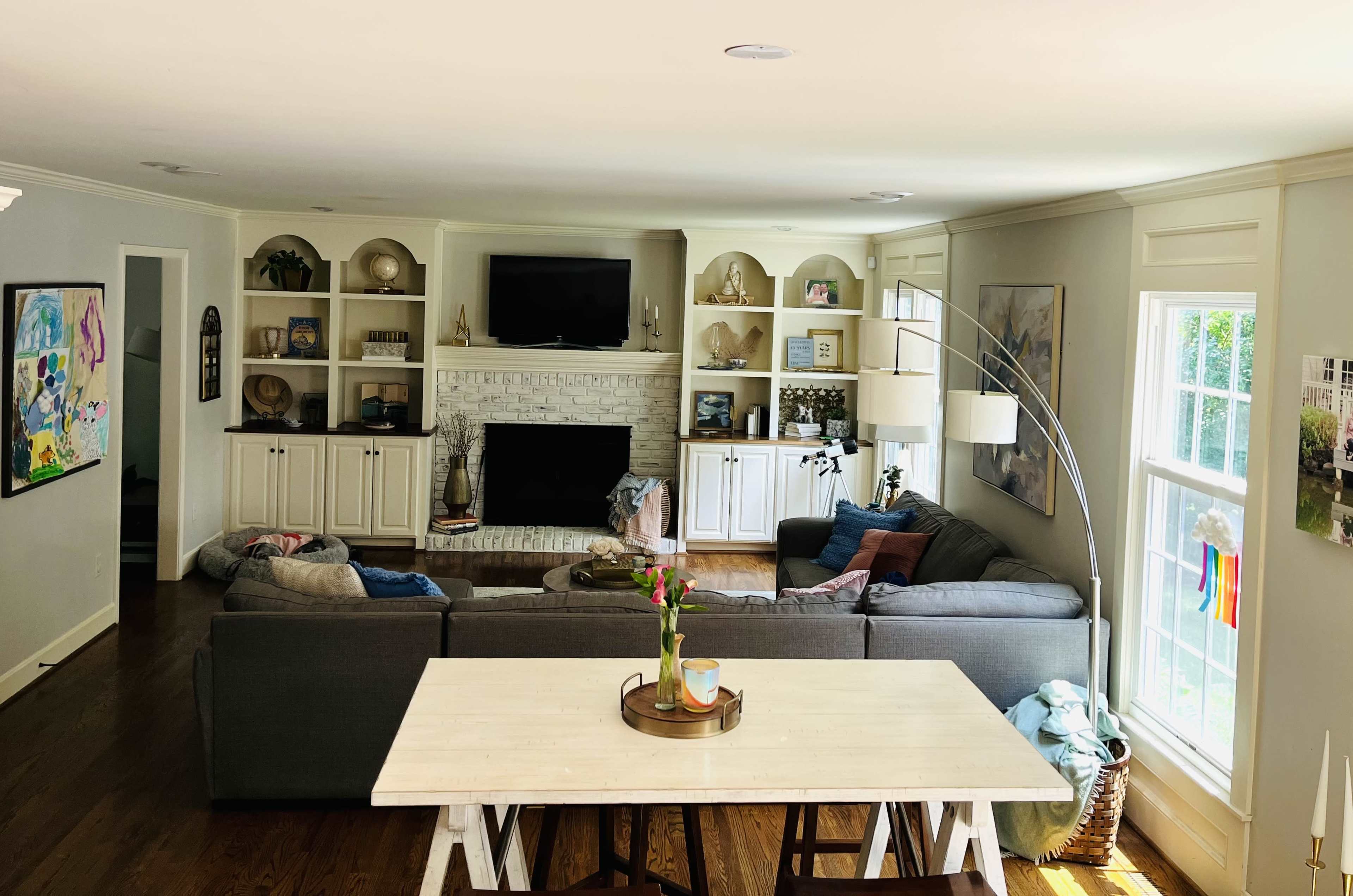 The image shows a living room with a large gray sectional sofa, a coffee table, and a white brick fireplace surrounded by shelves.