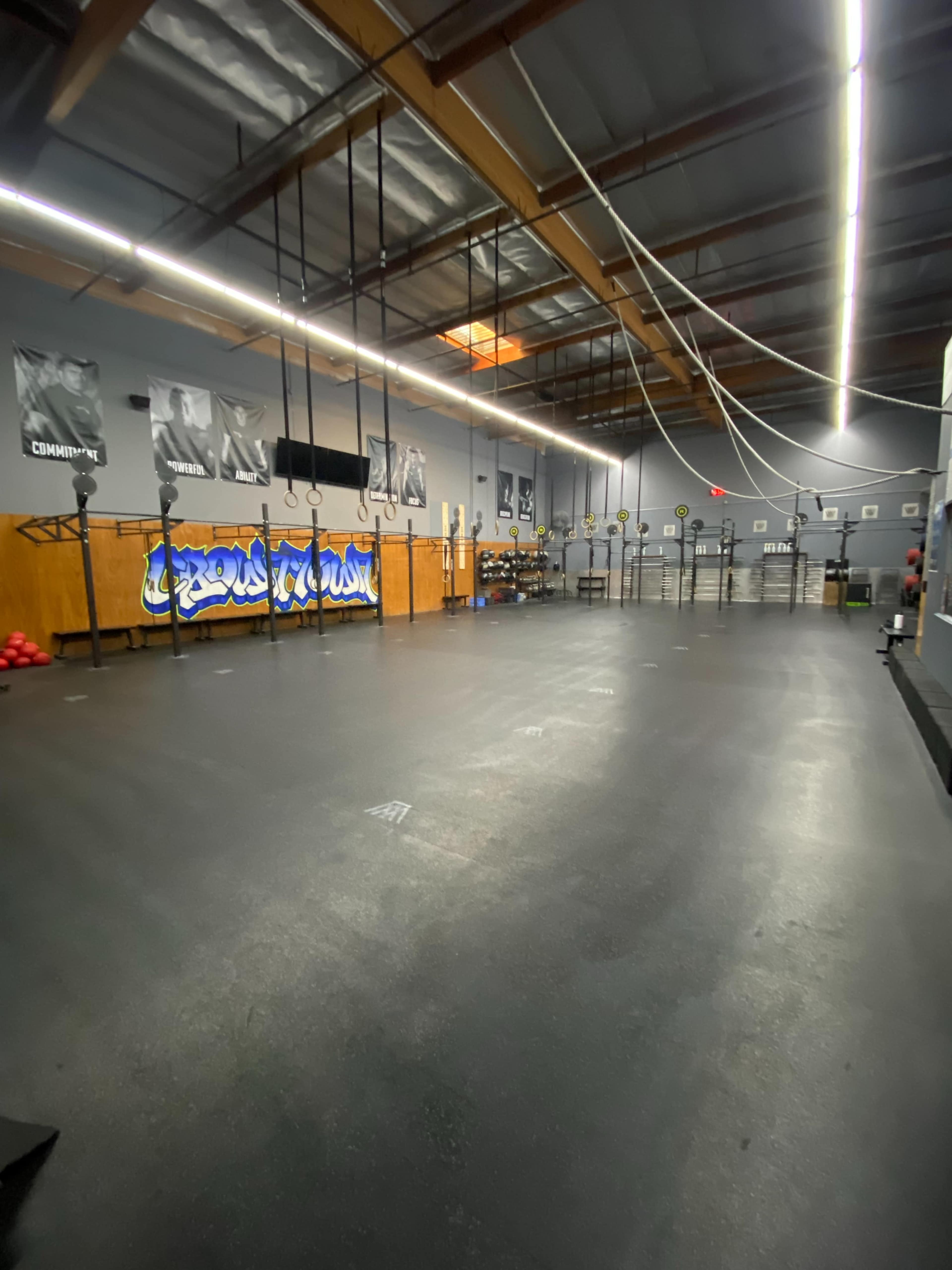 An empty gym interior with workout equipment, wall-mounted ropes, and a mural on the wall.