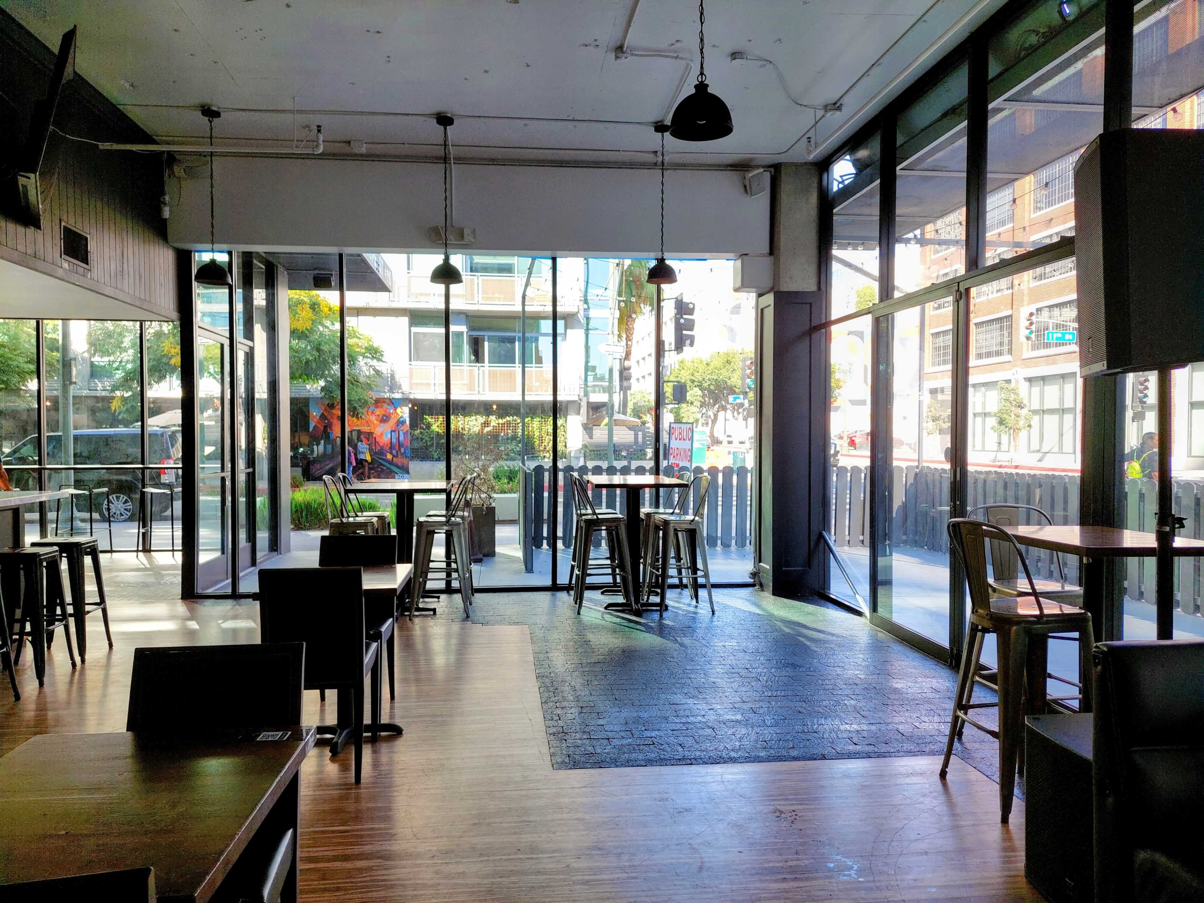 An empty café with large windows and a mix of high tables and chairs, allowing natural light to fill the space.
