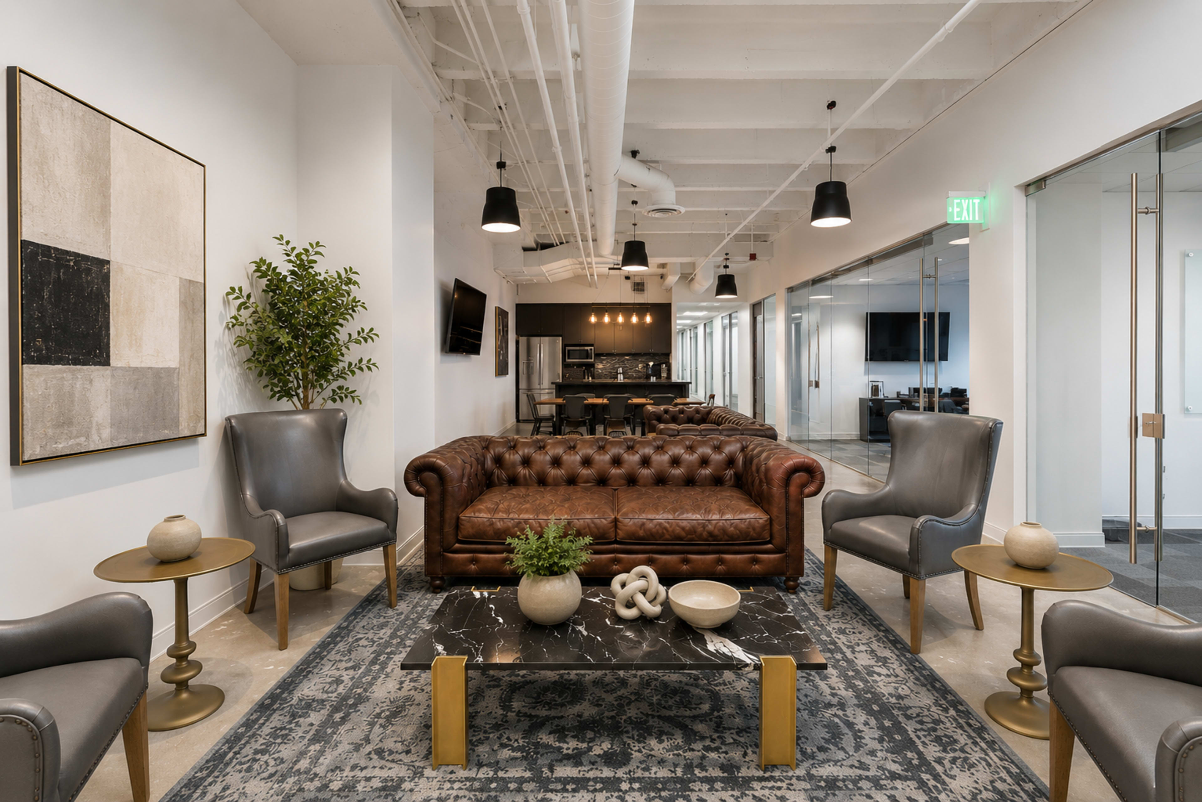 The image shows a modern office lobby with a brown leather chesterfield sofa, gray armchairs, a dark marble coffee table, and a series of glass-walled conference rooms in the background.