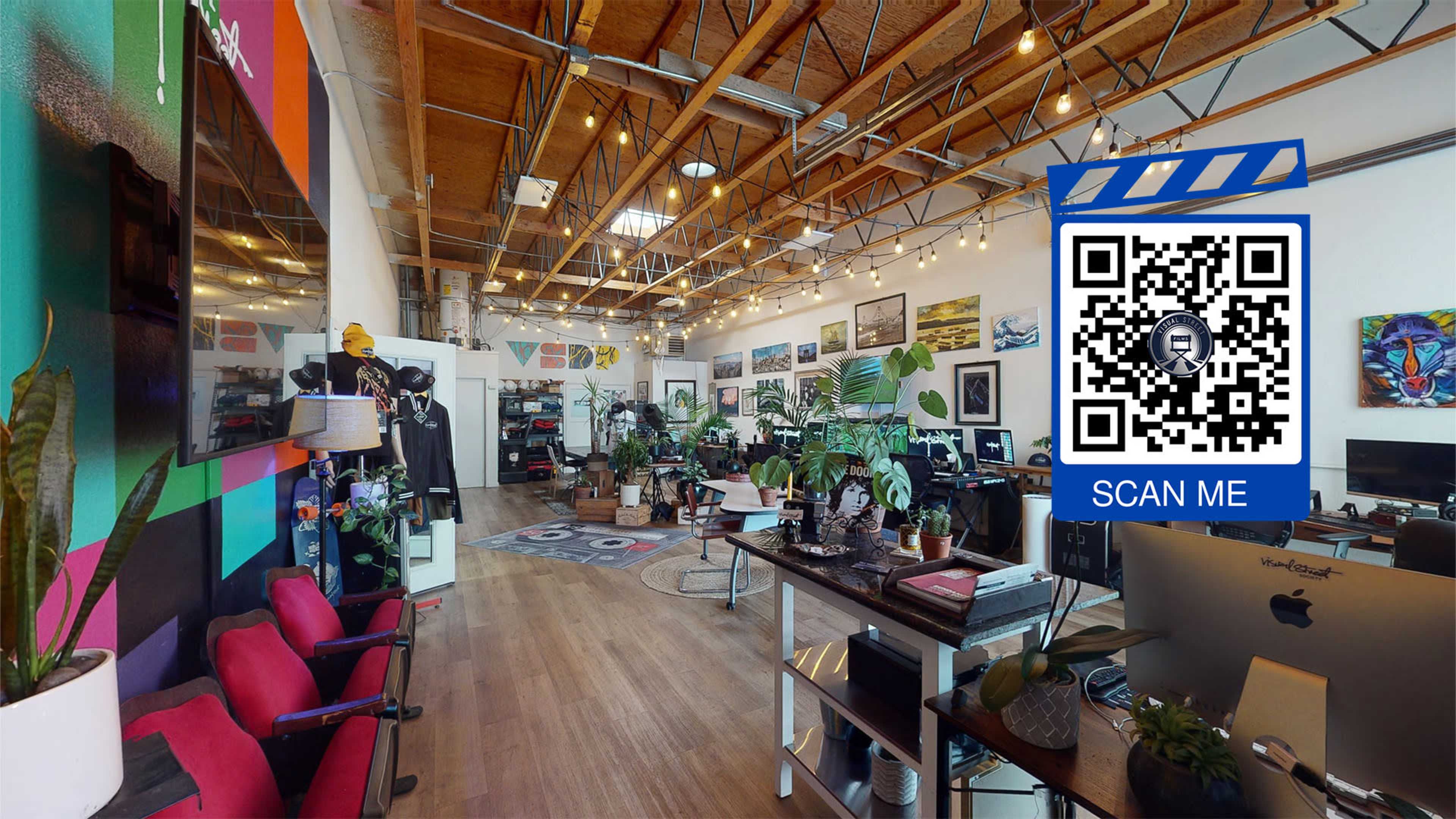 An interior of a spacious office or studio with wooden beams, various artwork on the walls, plants, and workstations.