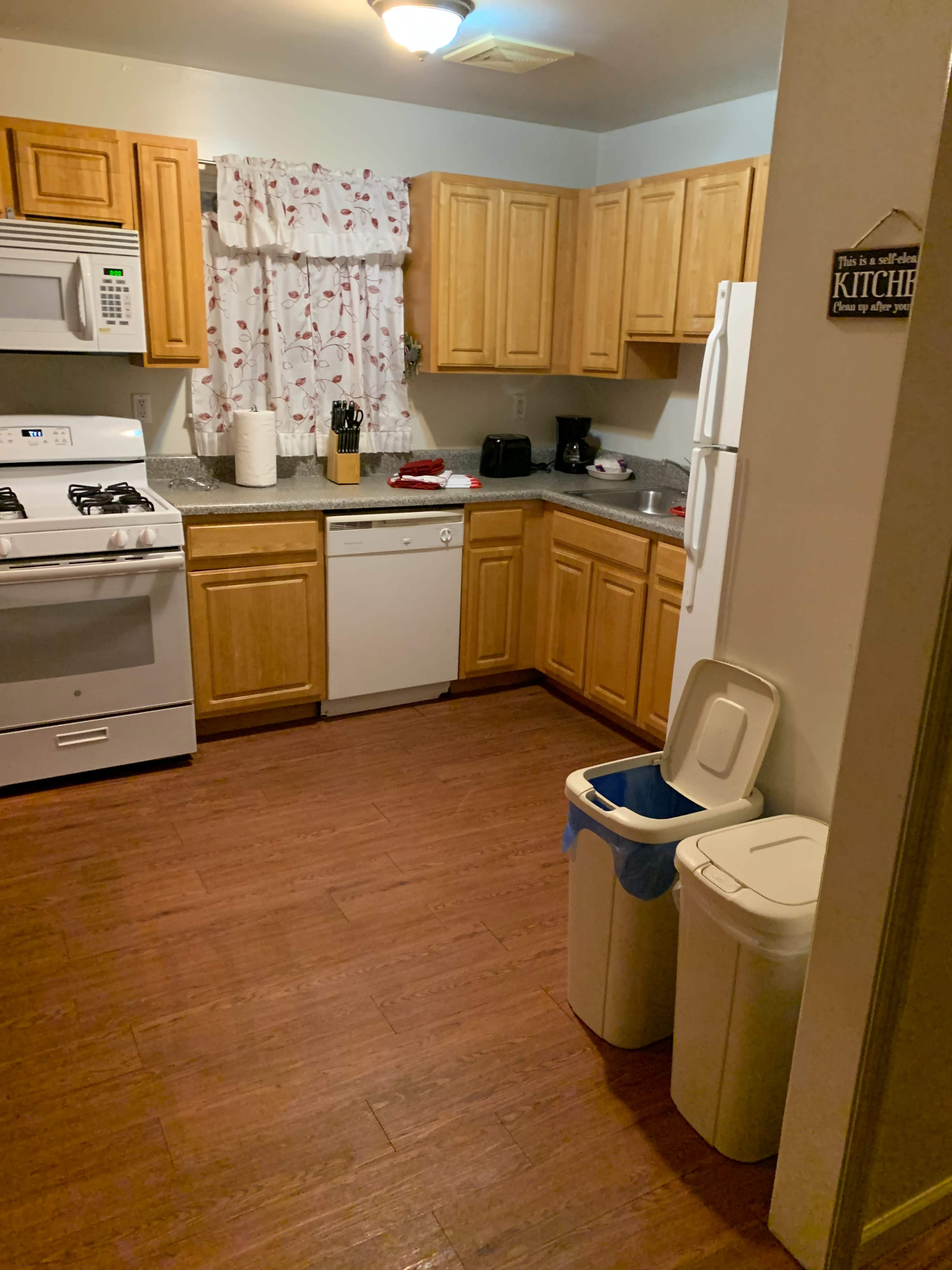 A kitchen with wooden cabinetry, a gas stove, and a dishwasher, complemented by a countertop and two trash bins.