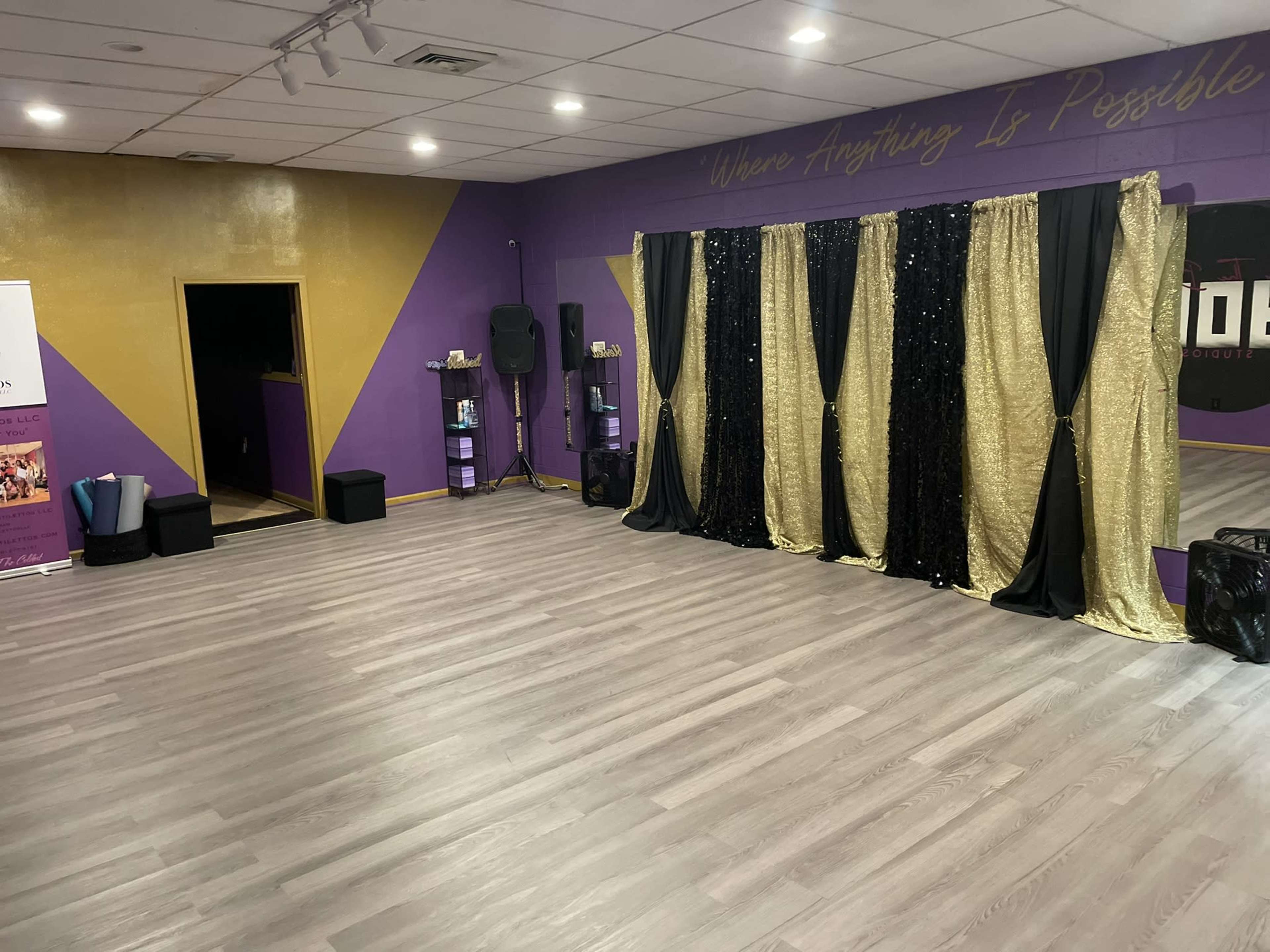 The image shows a spacious dance studio with a hardwood floor and a backdrop of black and gold sequined curtains against a purple wall.