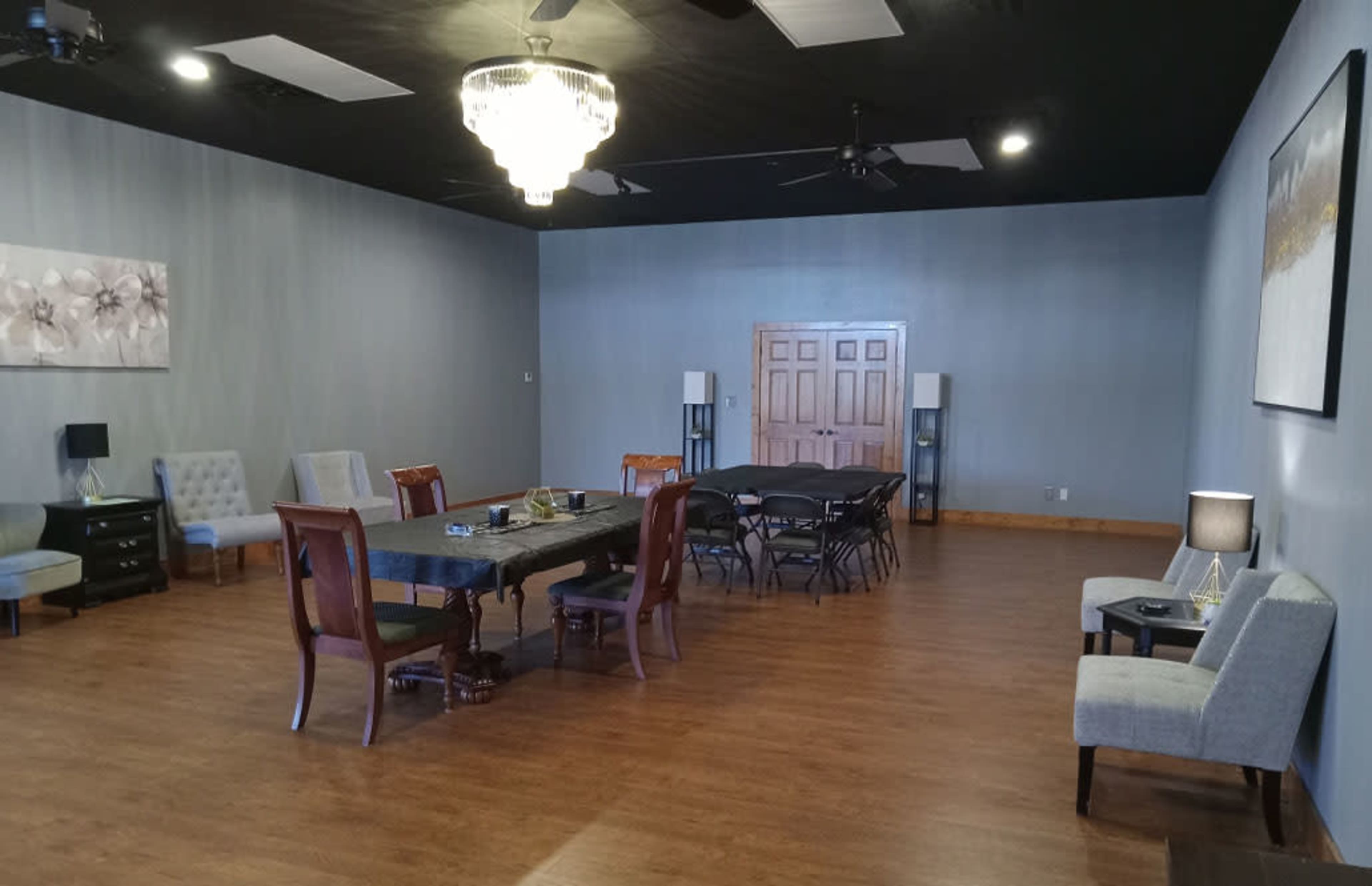 The room features a large rectangular table surrounded by chairs, with additional seating along the walls and a chandelier overhead.