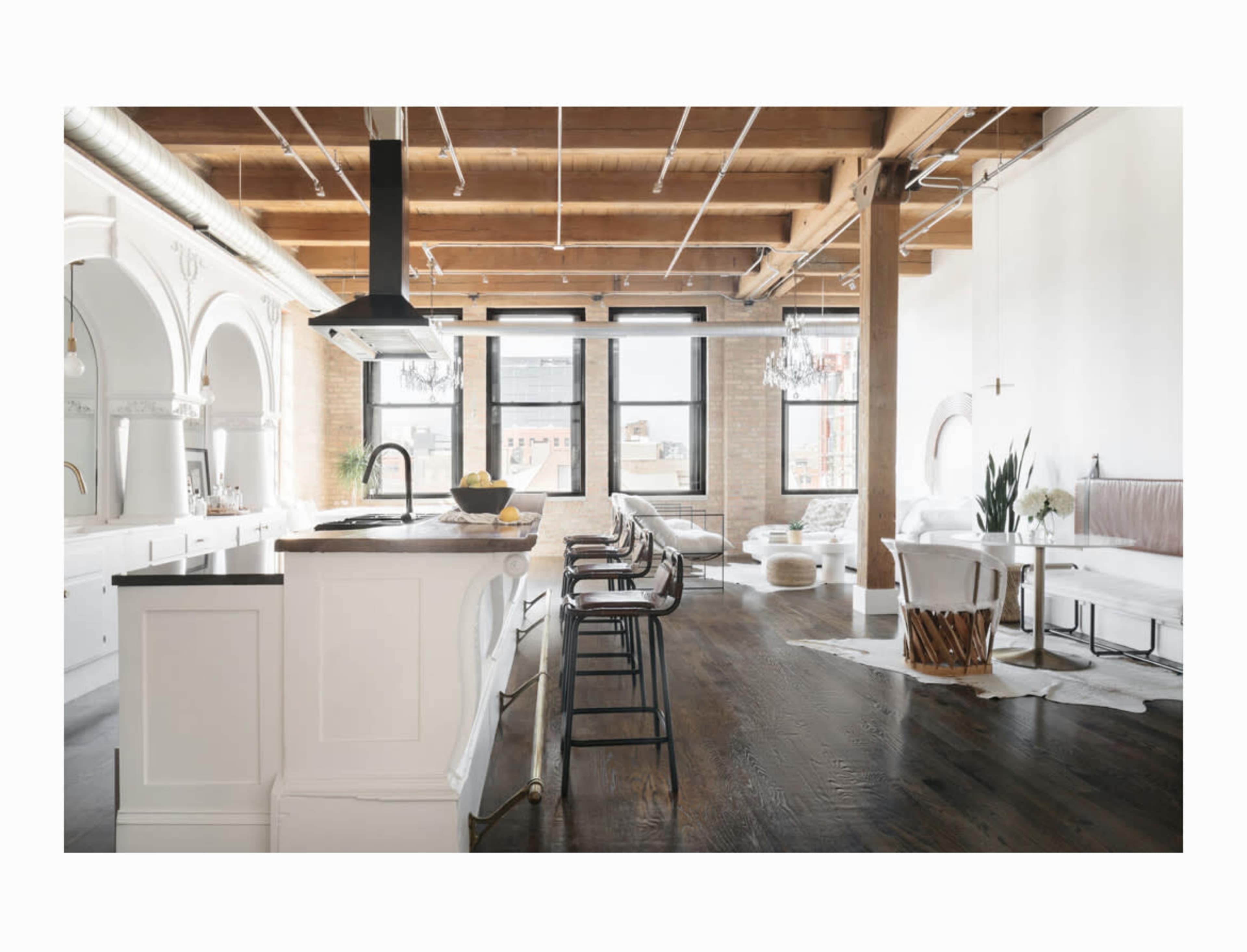 A spacious, modern loft features a kitchen island with bar stools, large windows allowing natural light, and a mix of seating areas.