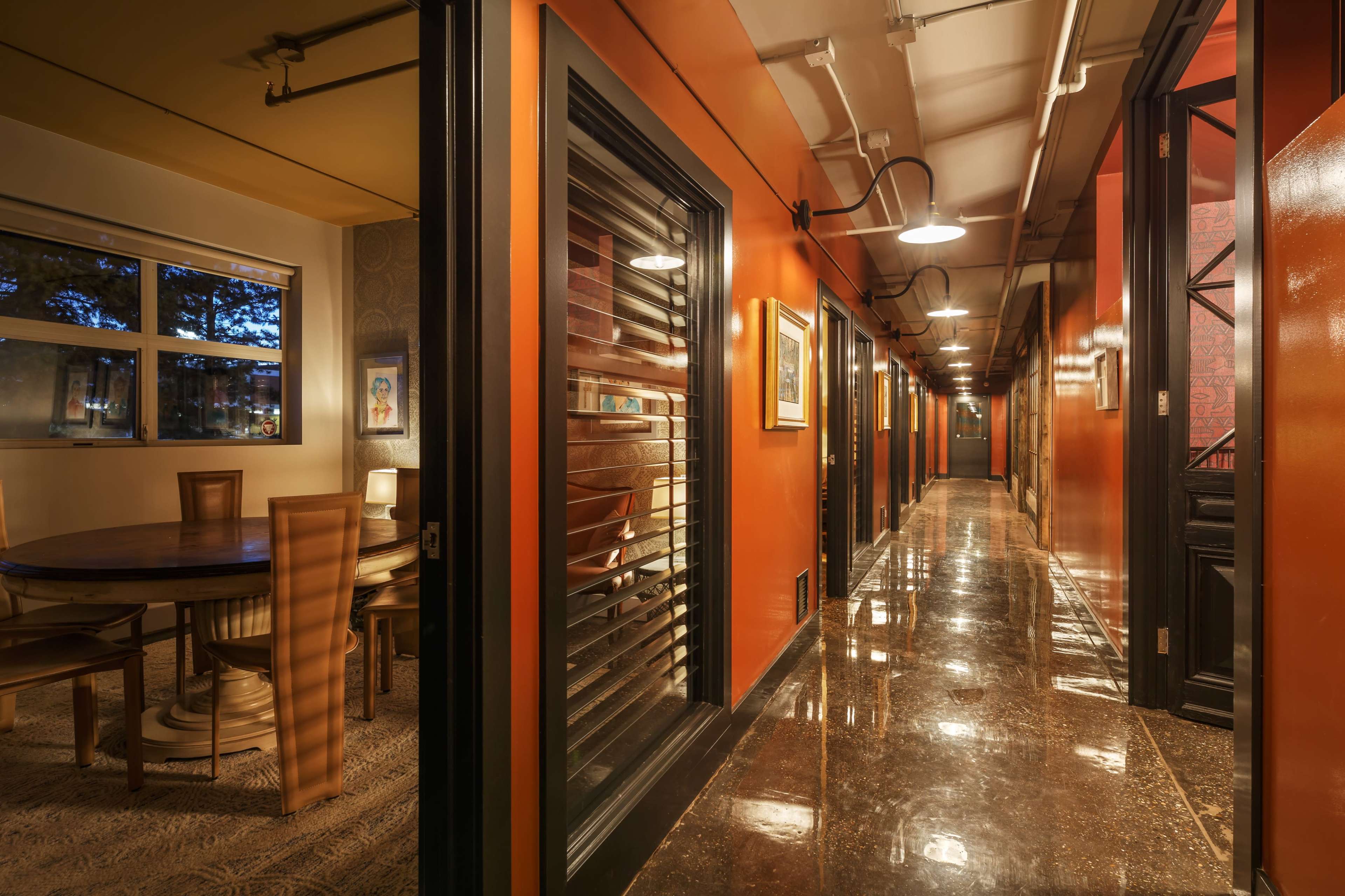 A corridor with dark walls, polished flooring, and accessible rooms on either side, leading to a dining area at the end.