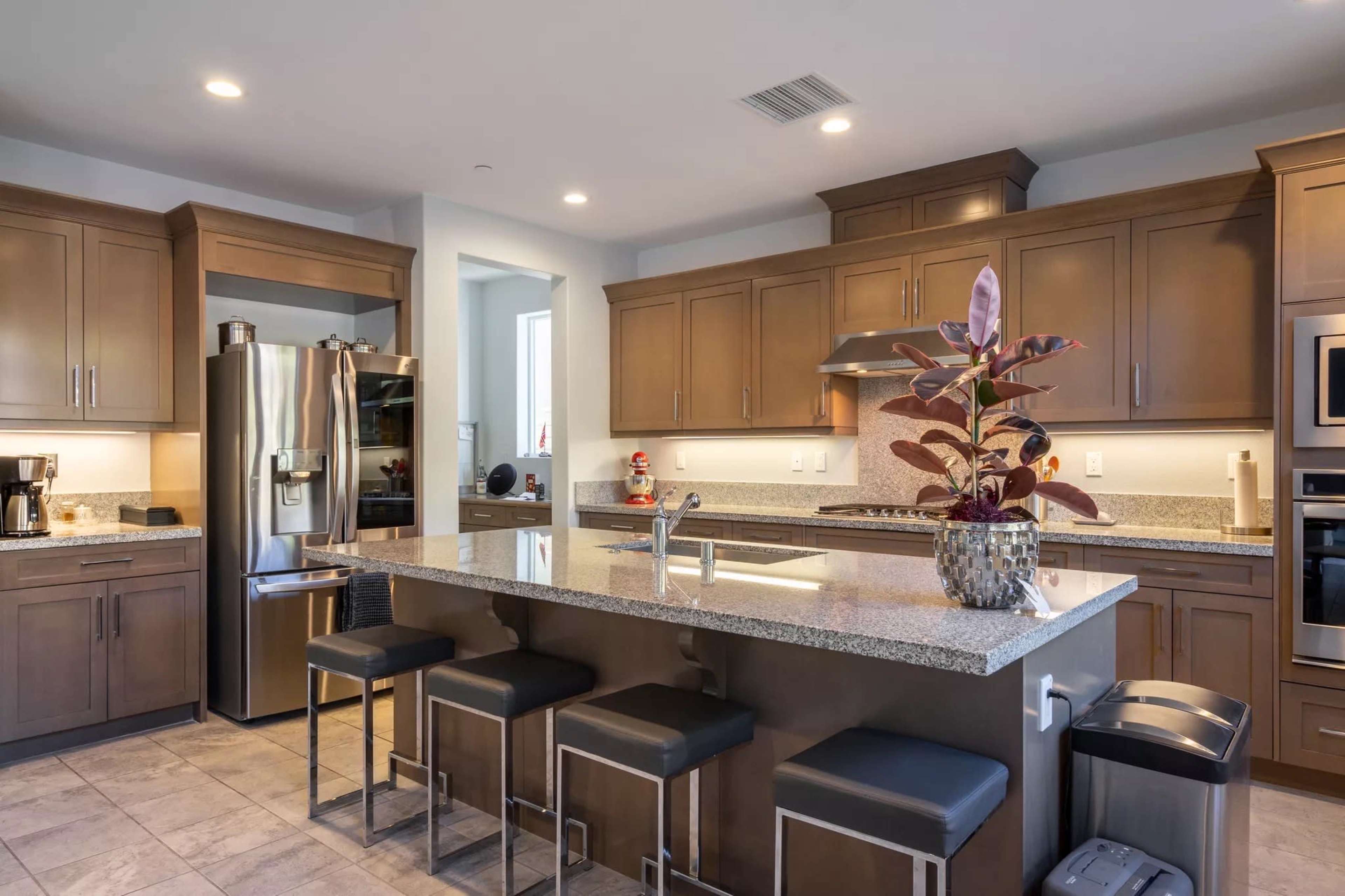 The kitchen features wooden cabinets, stainless steel appliances, a central island with bar stools, and a potted plant.