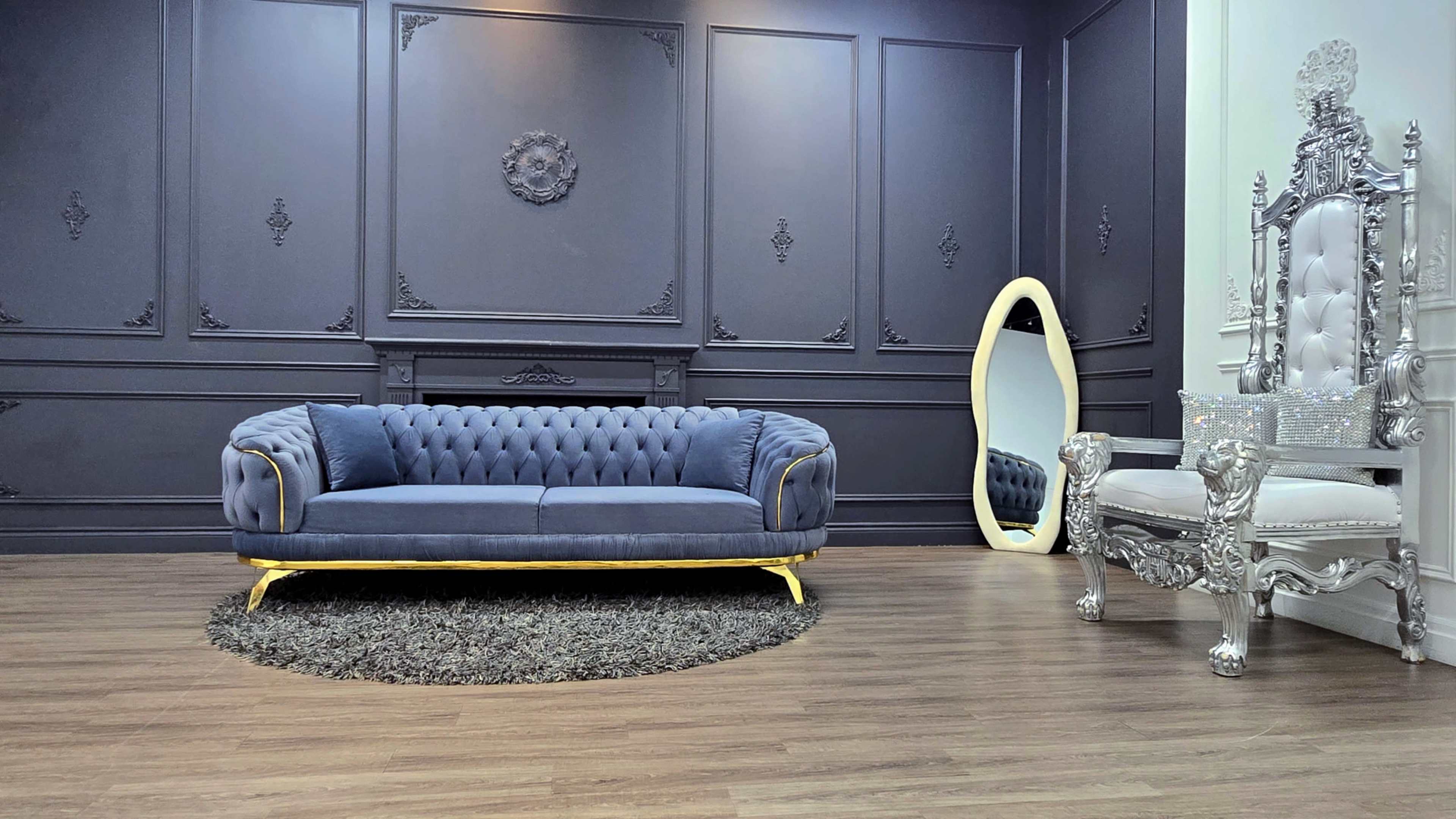 The image shows a luxurious sitting room featuring a dark wall, a velvet blue sofa with gold accents, a decorative silver mirror, and an ornate silver chair.