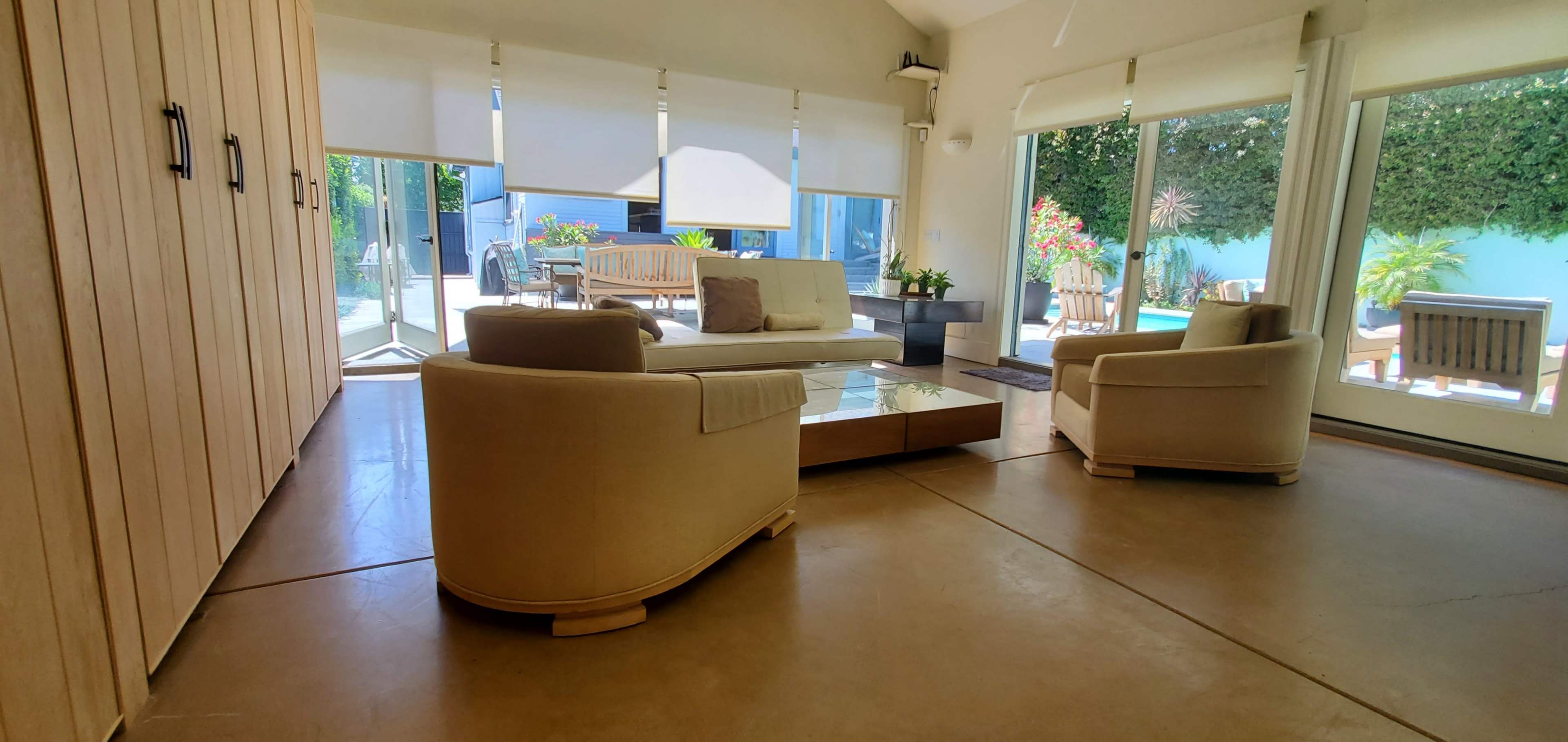 A modern living room with beige furniture, large windows, and a view of a garden area outside.