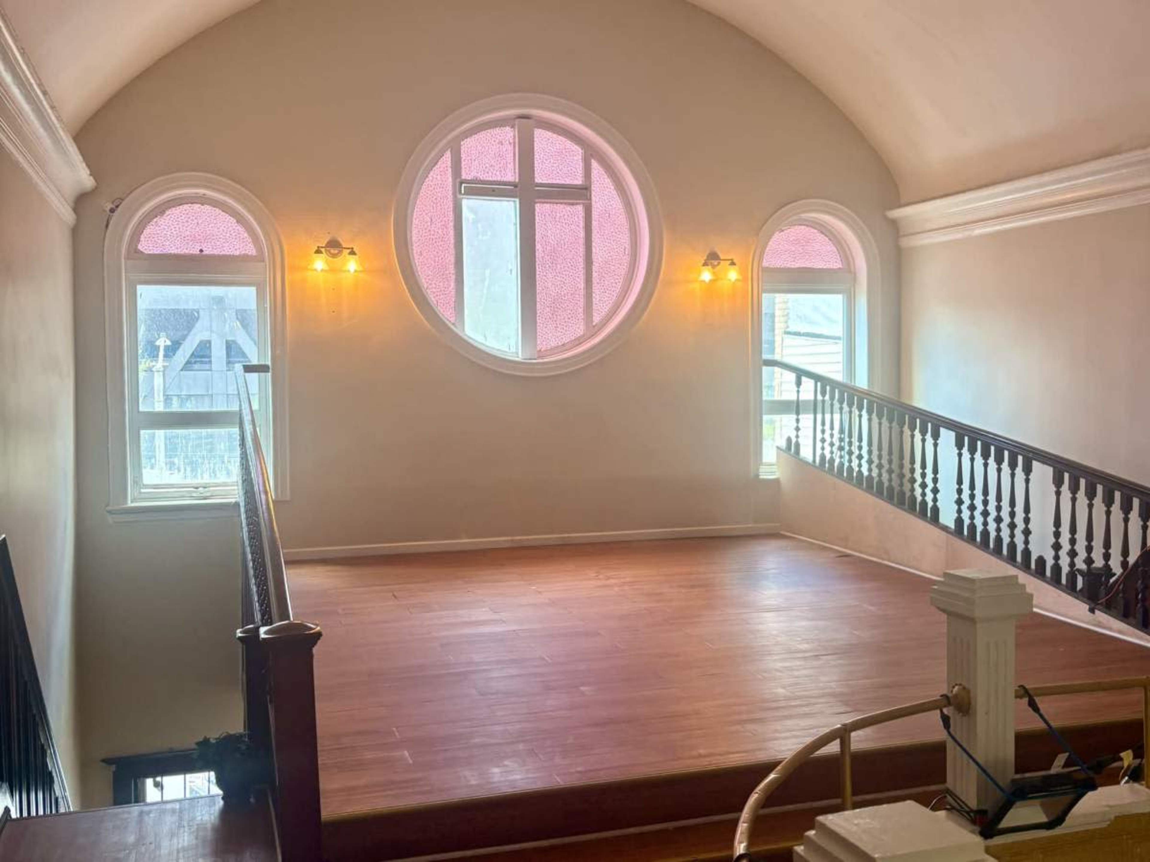 The image shows a spacious landing area with a circular window and wooden flooring, flanked by two smaller windows and illuminated by wall sconces.