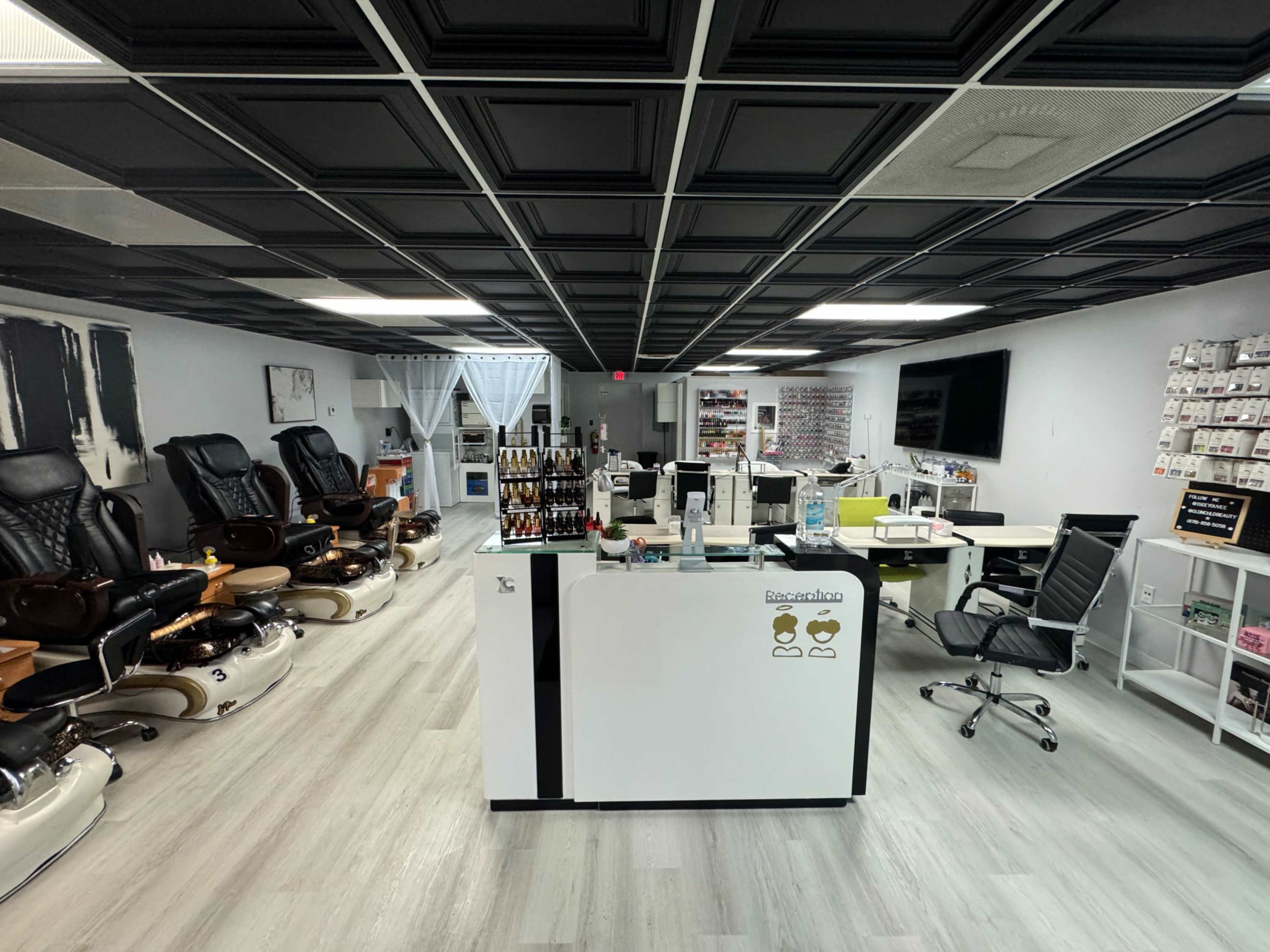 The image shows a modern nail salon with a reception desk, several pedicure chairs, and a well-organized display of nail products.