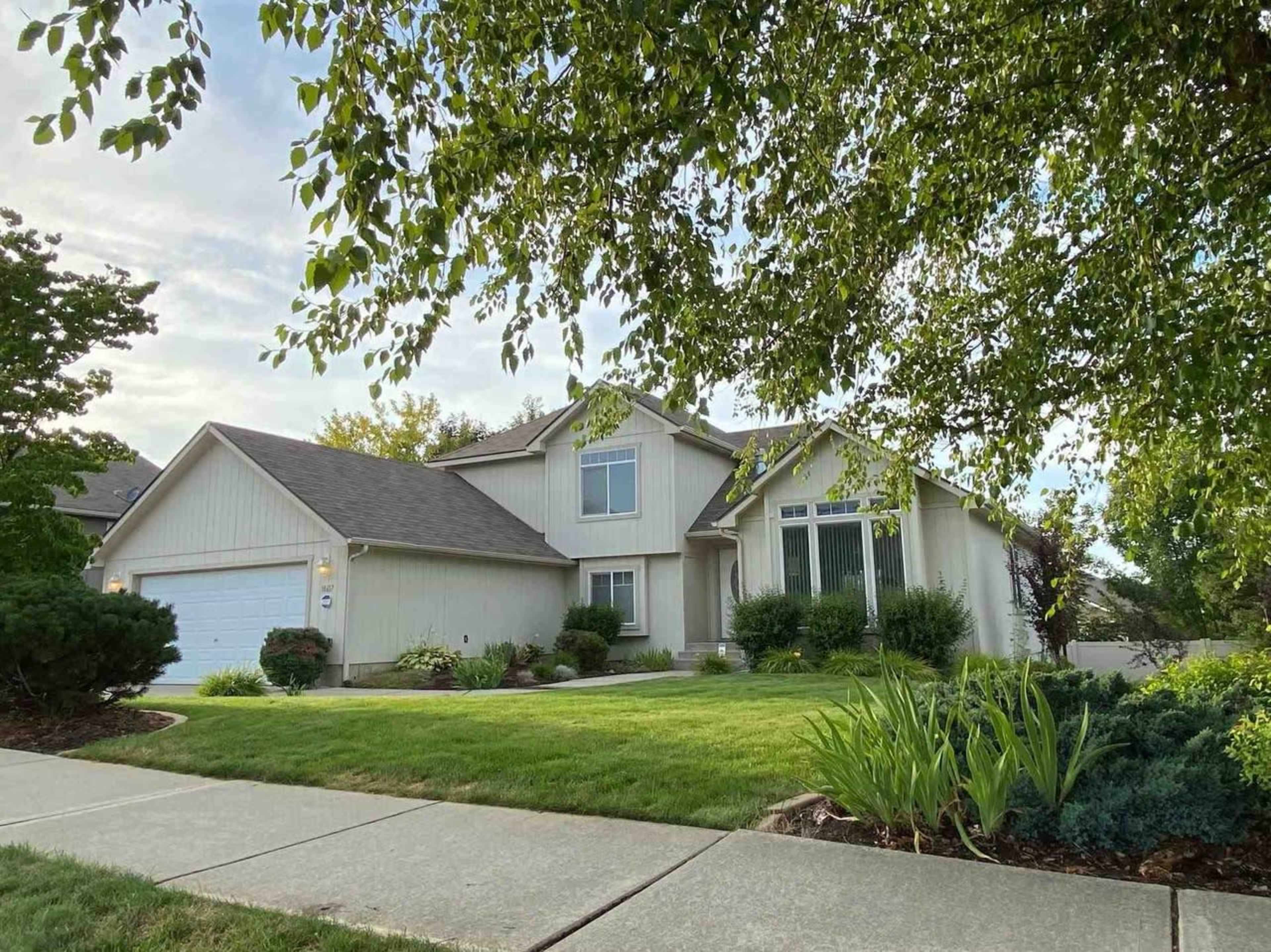 A two-story house with a gray exterior, large windows, and a manicured lawn is shown on a residential street.
