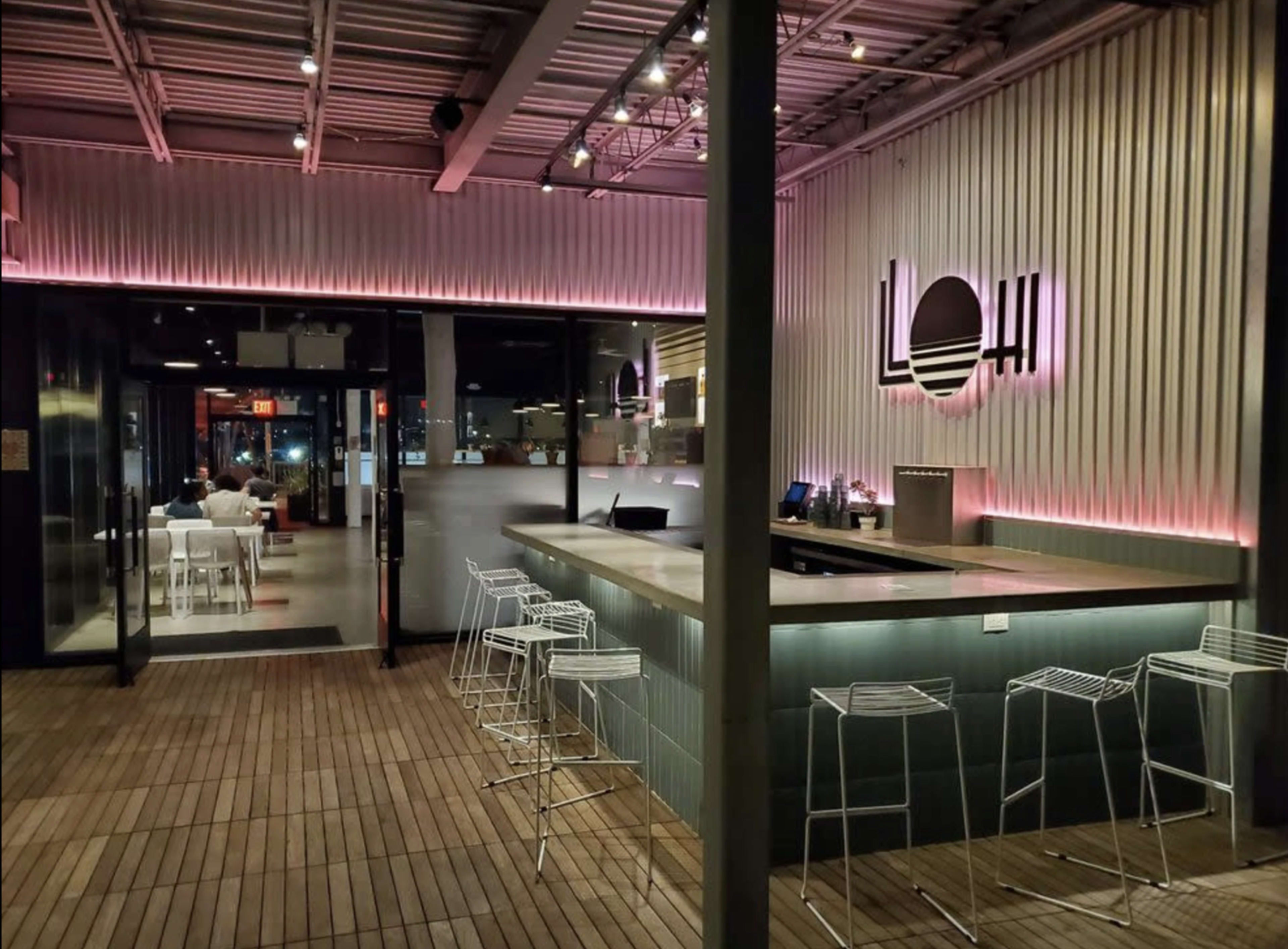 The image shows a modern bar interior with a sleek counter, contemporary seating, and ambient lighting in a warm tone.