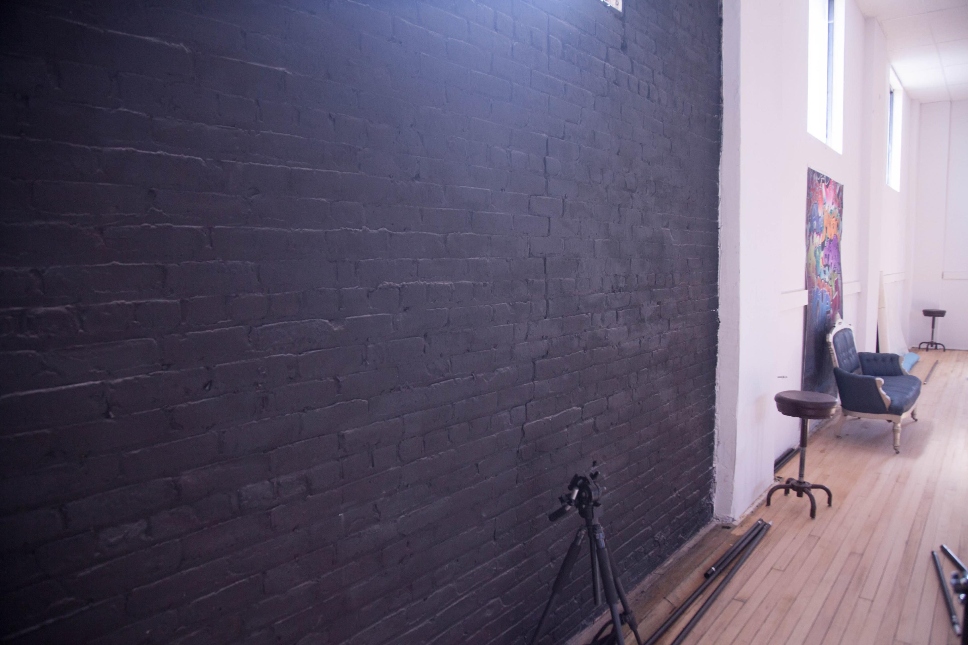A spacious room with a black brick wall, hardwood flooring, a blue seating area, and a tripod on the floor.