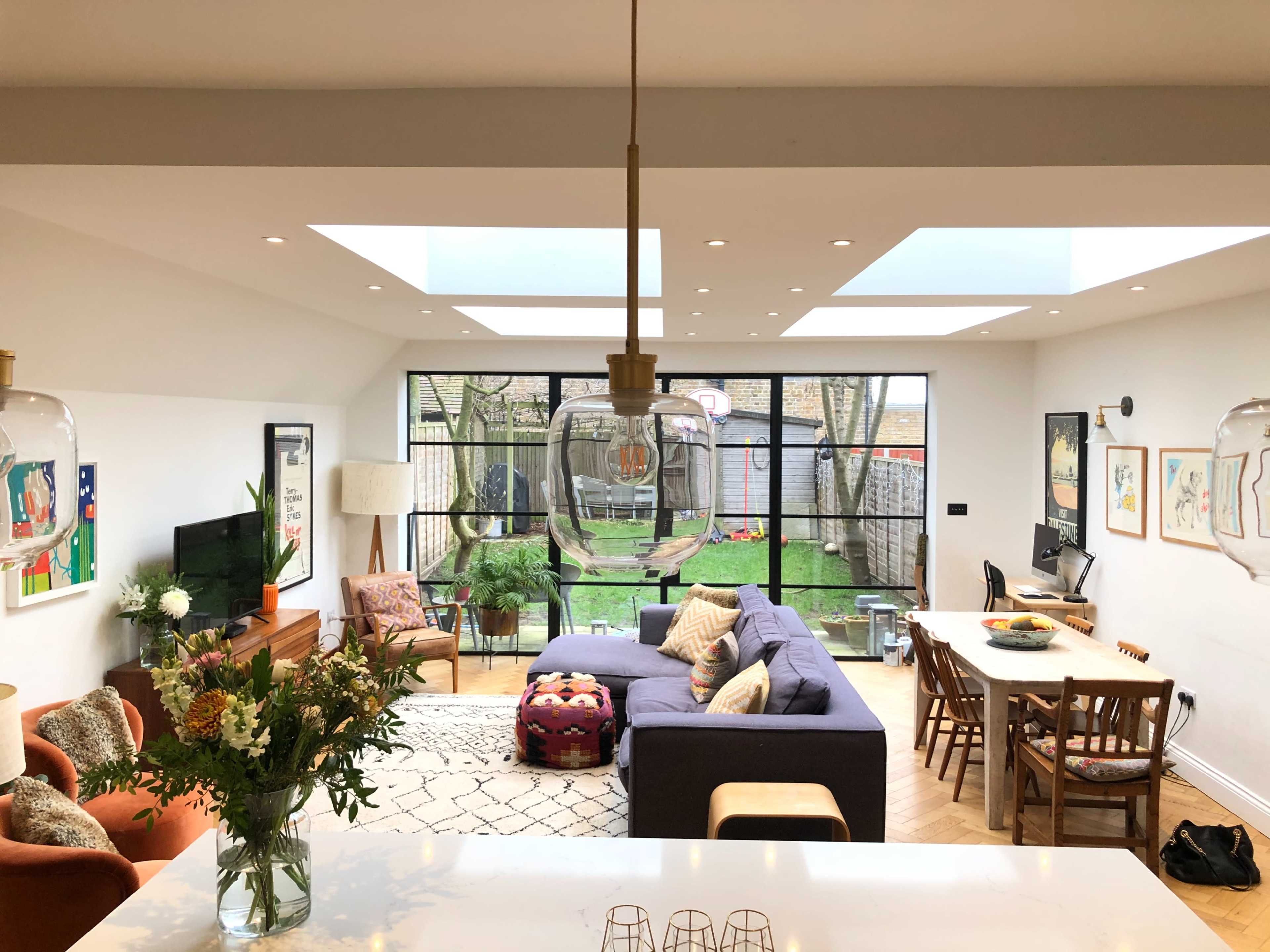 A spacious living area features a blue couch, a dining table, and large skylights that illuminate the space.