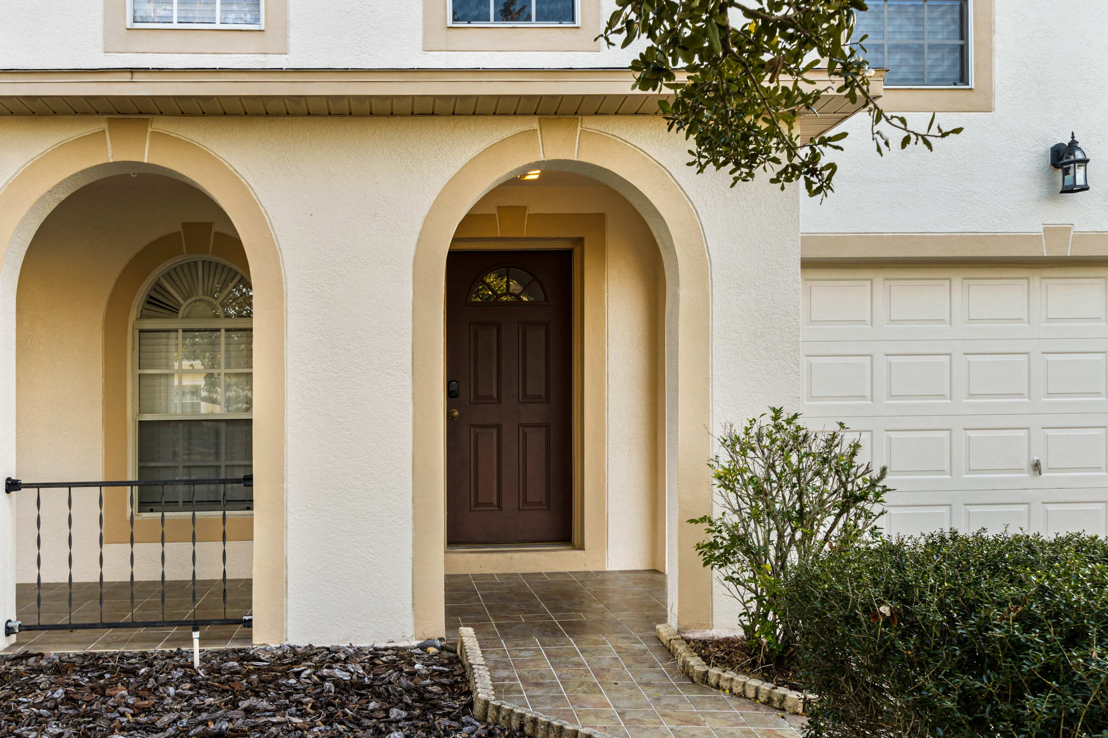 The entrance of a house with arched doorways, a brown front door, and a two-car garage visible in the background.