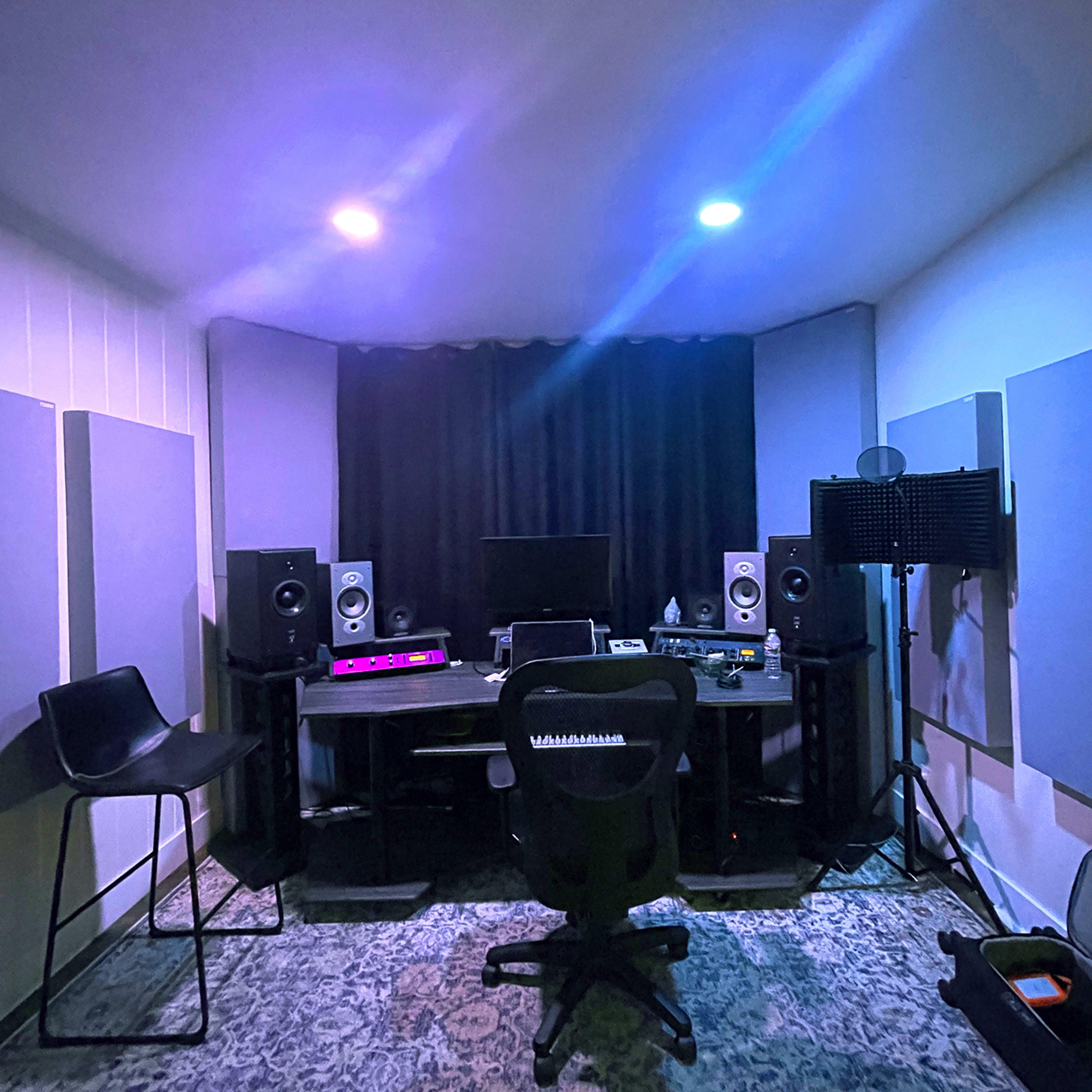 The image shows a music studio with a desk, computer monitor, speakers, and soundproofing panels on the walls.