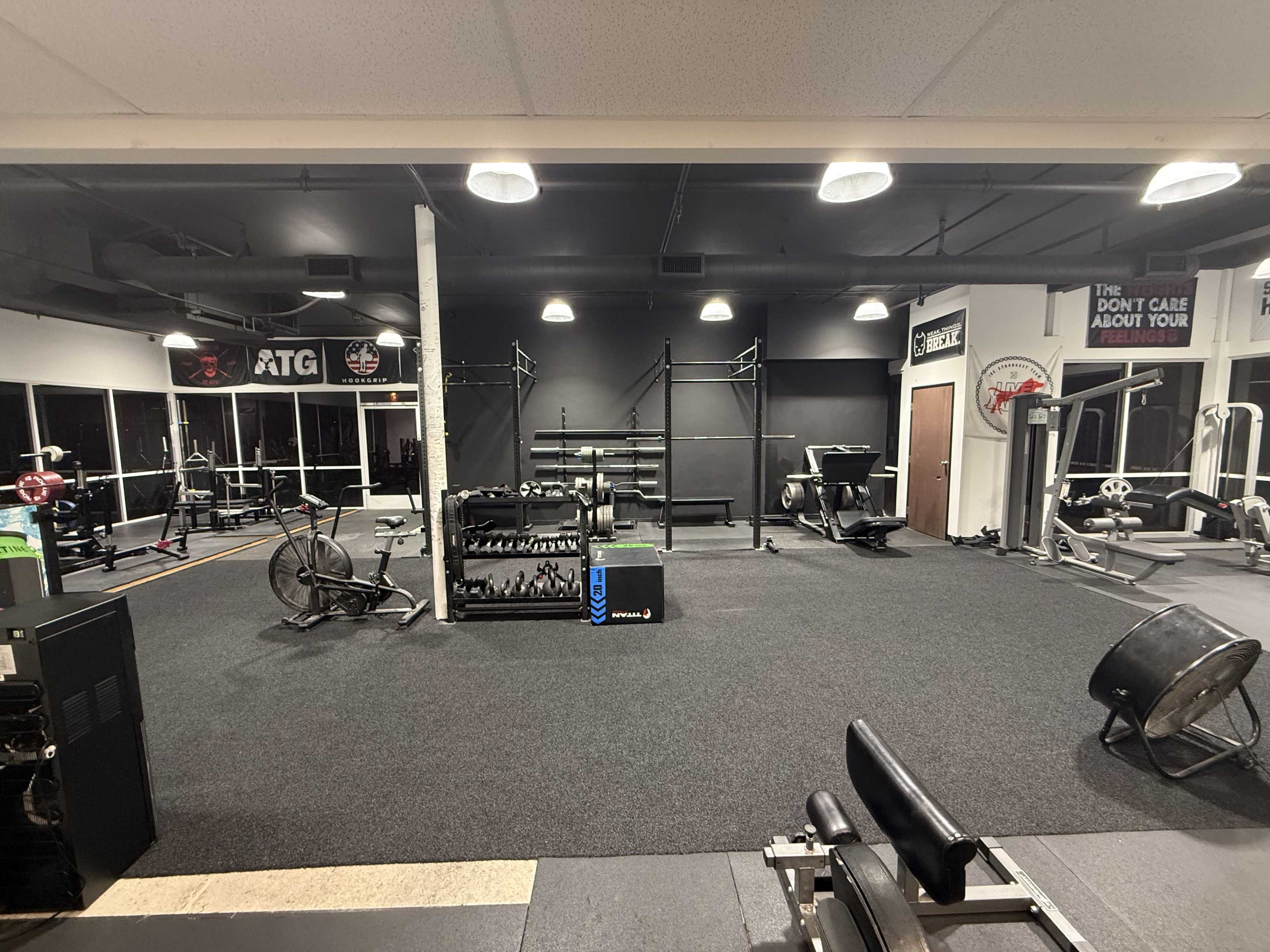 The image shows a spacious gym area equipped with various exercise machines, weights, and large windows allowing for natural light.