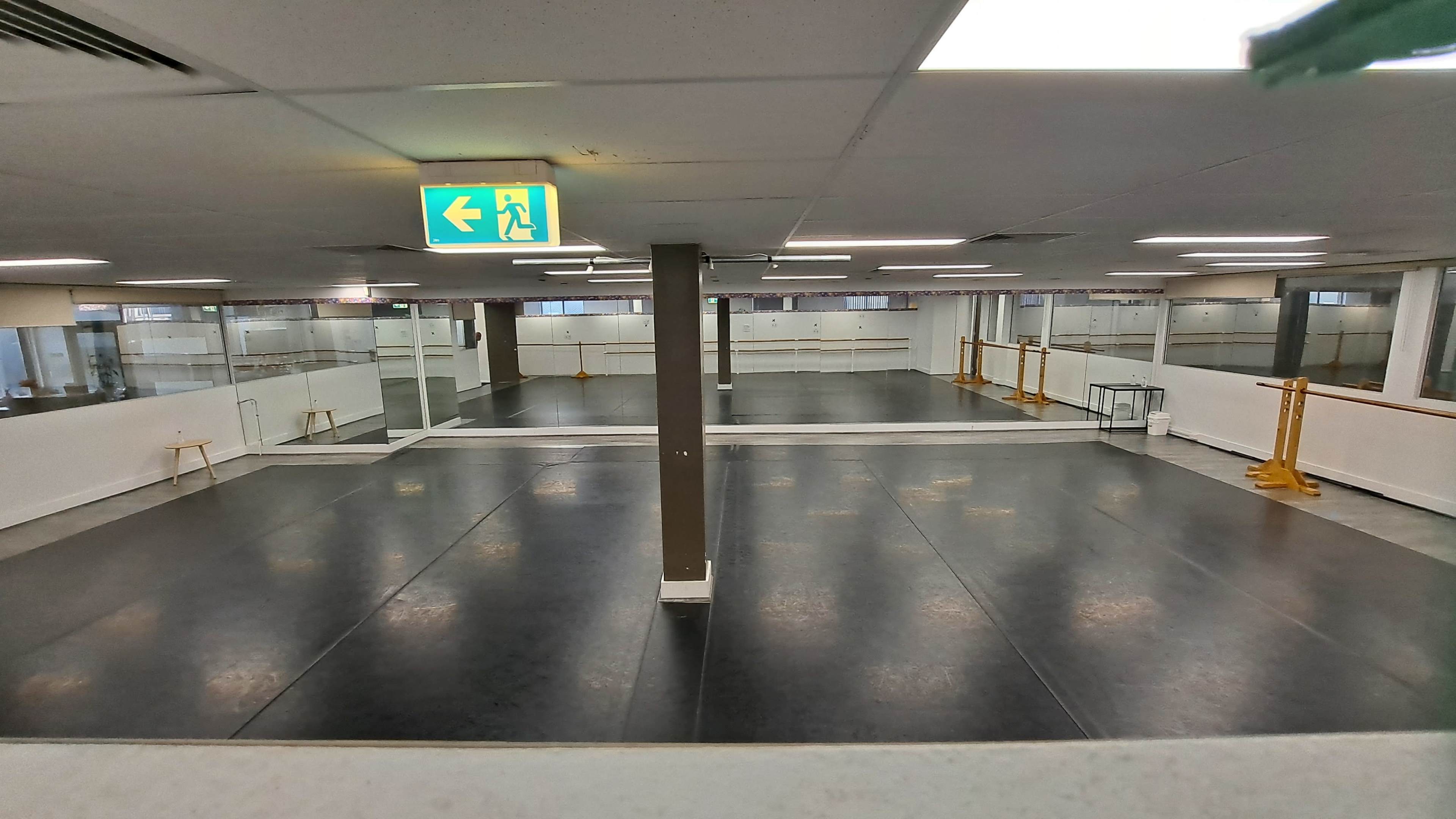 An empty dance studio with mirrored walls and wooden ballet barres along the sides.