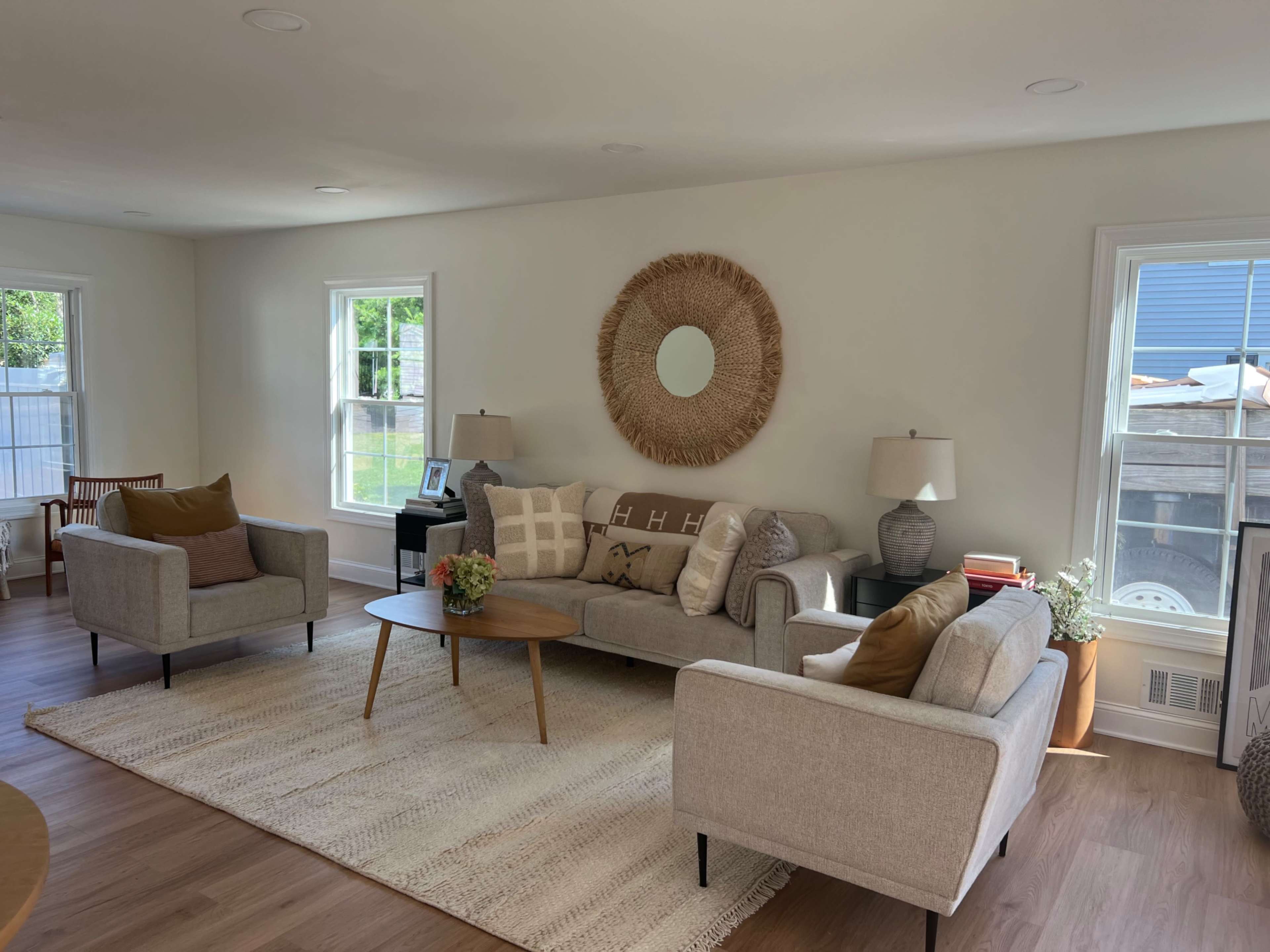 A bright, modern living room furnished with a gray sofa, two armchairs, and a round wooden coffee table, all arranged on a textured rug.