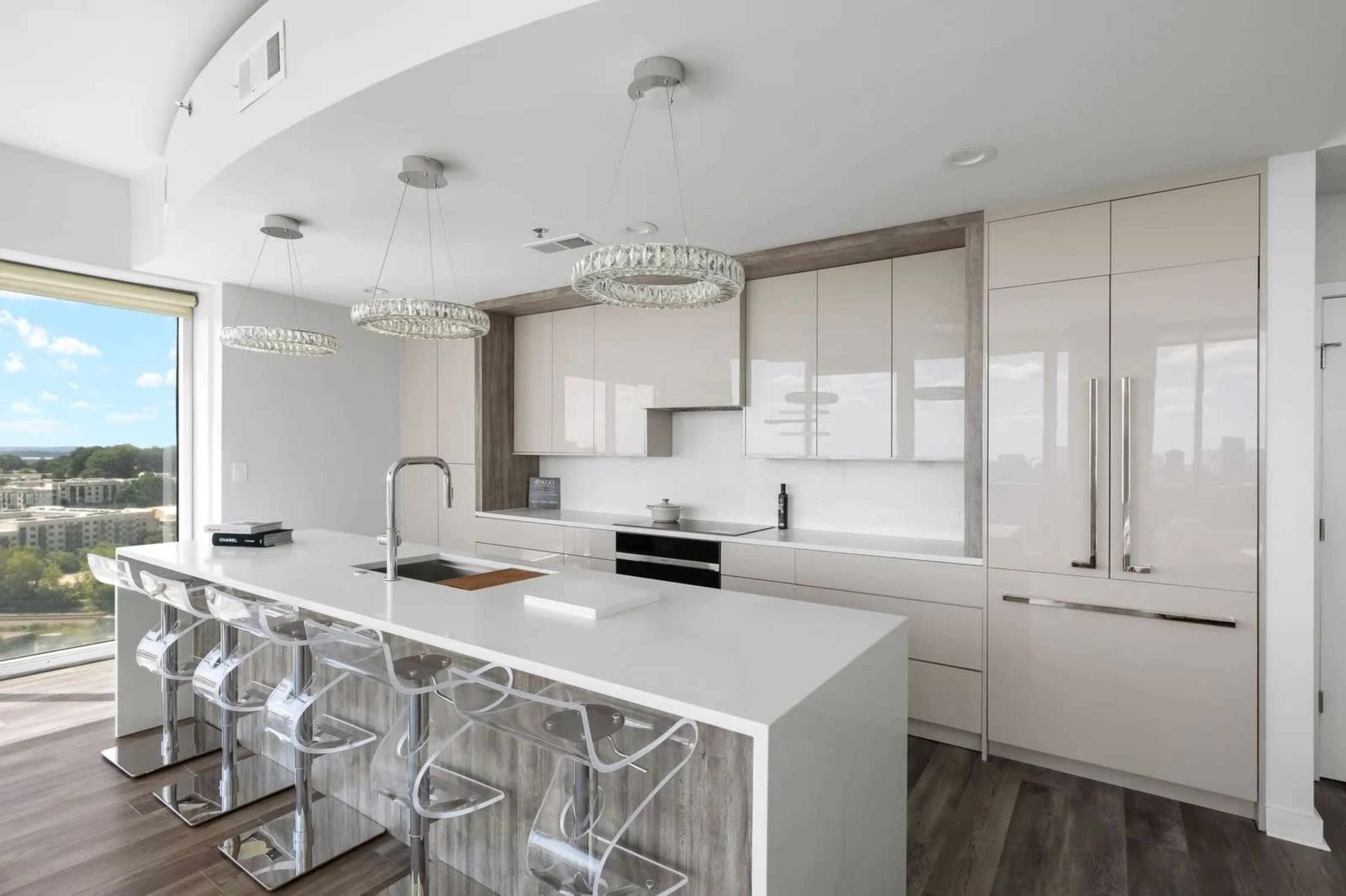 The image shows a modern kitchen with sleek cabinetry, a large island with bar stools, and pendant lighting.