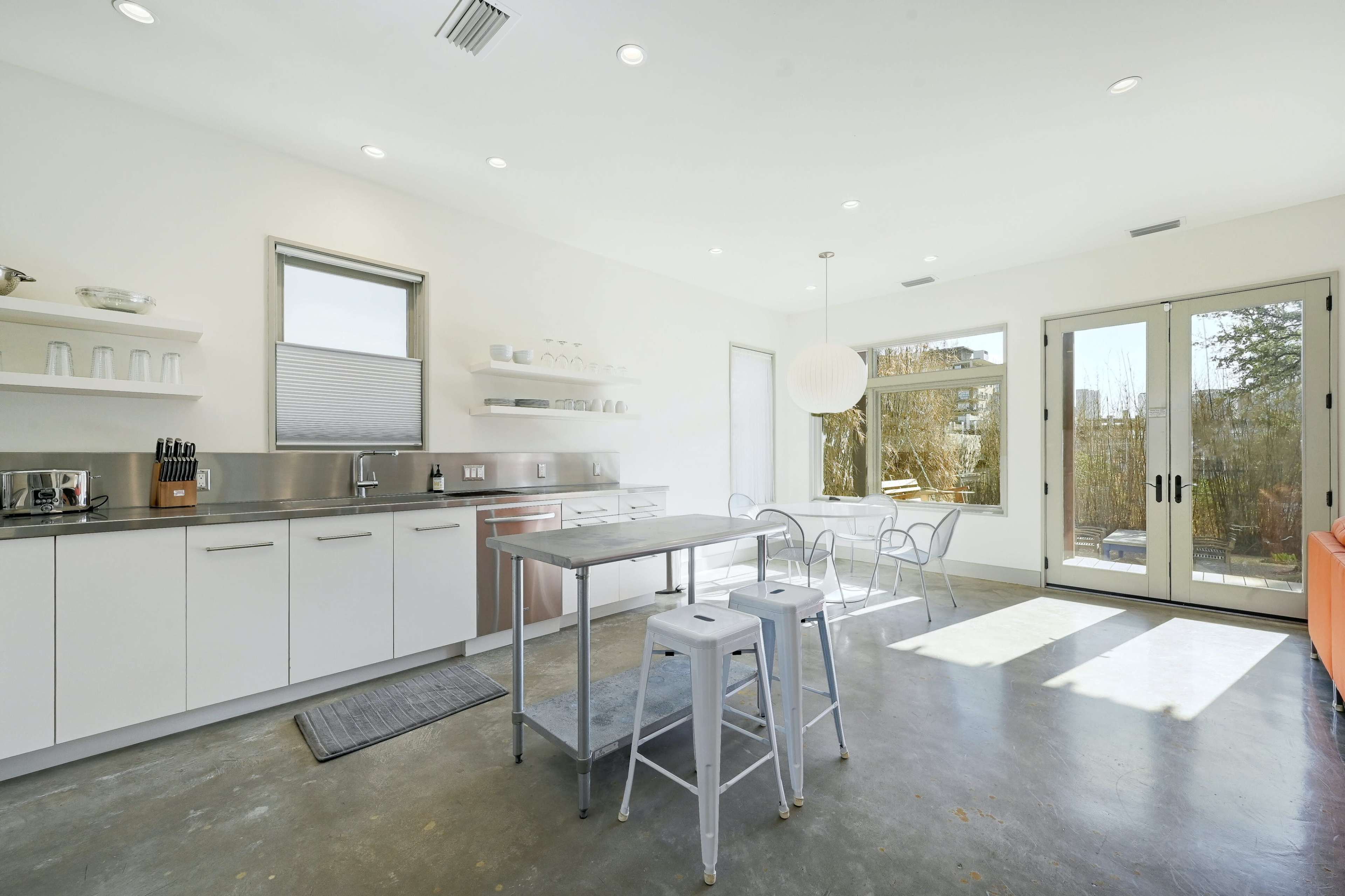 A bright, modern kitchen features stainless steel appliances, white cabinetry, and large glass doors leading to an outdoor area.