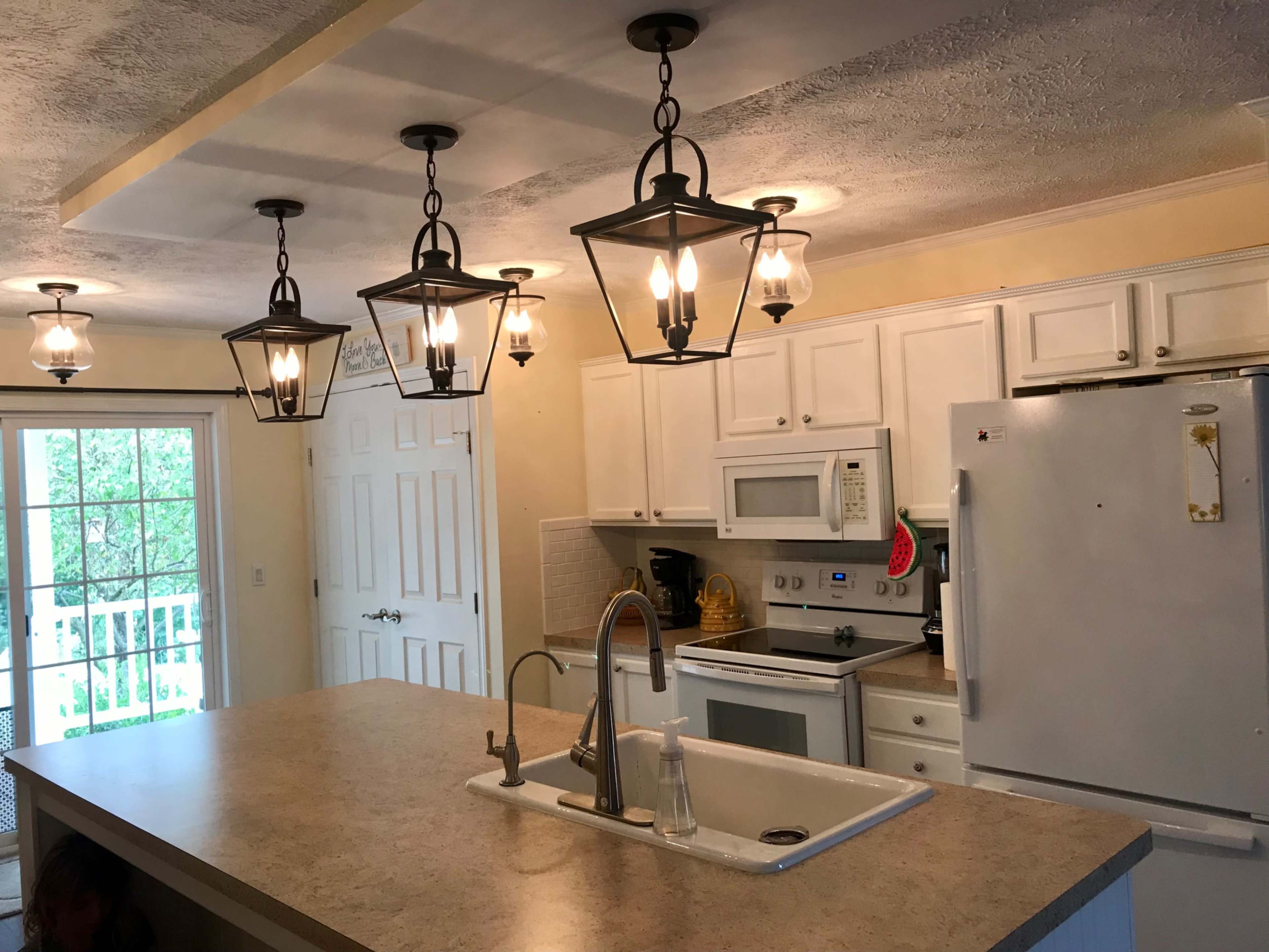 A kitchen with white cabinets, a central island featuring a sink, and multiple pendant lights hanging from the ceiling.