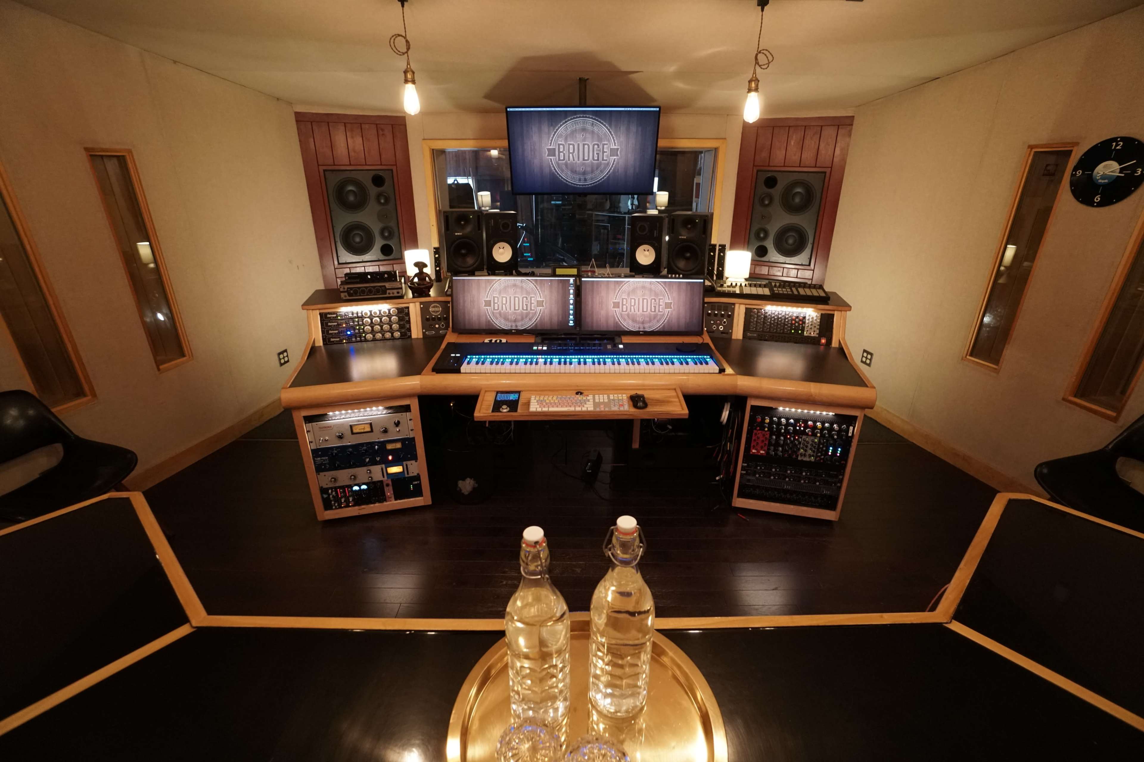 A recording studio equipped with sound mixing consoles, speakers, and a keyboard, featuring a central table with two bottles of water.