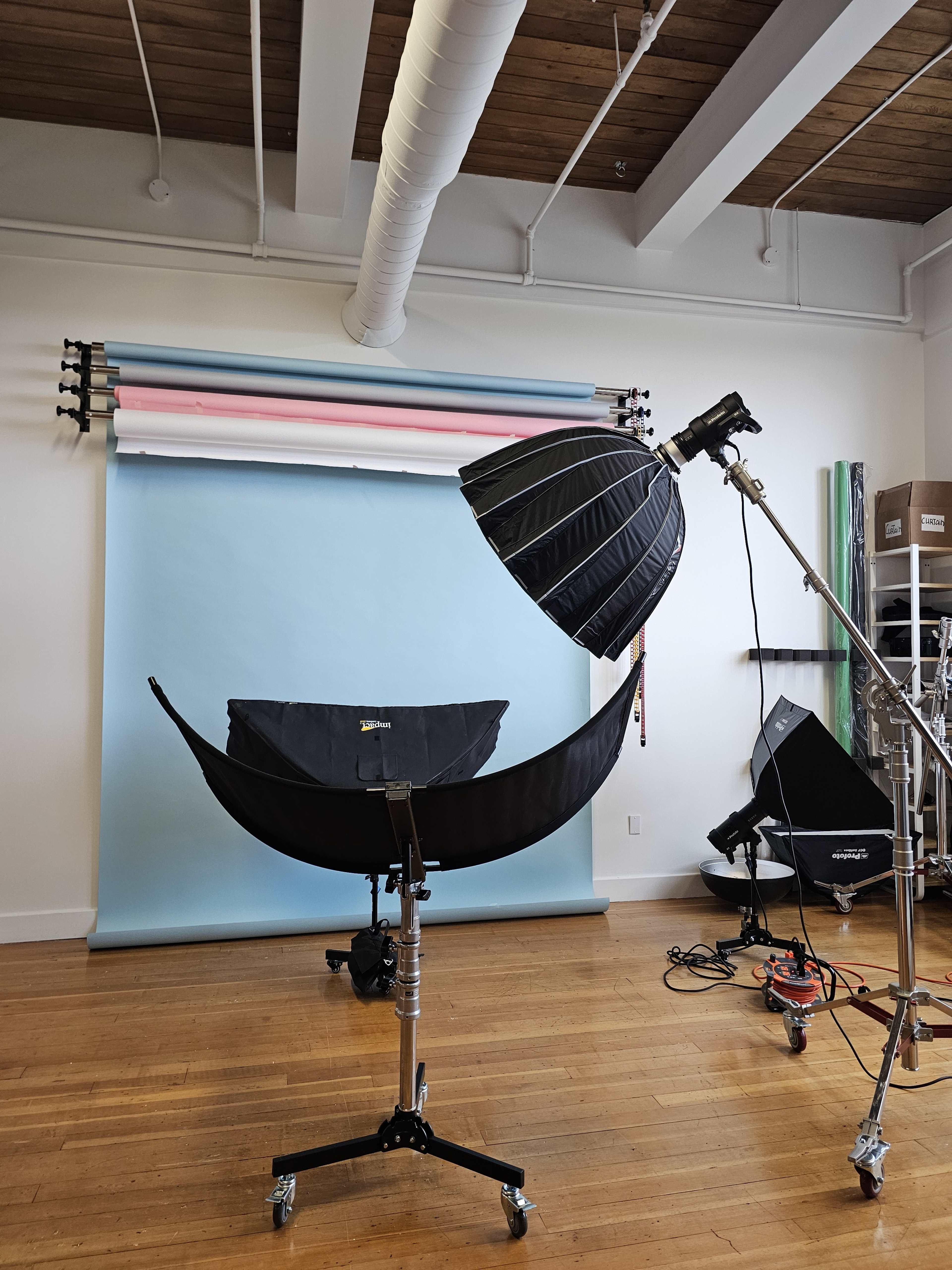 A photography studio with a large softbox light positioned next to a backdrop featuring pastel-colored rolls and various equipment arranged neatly.