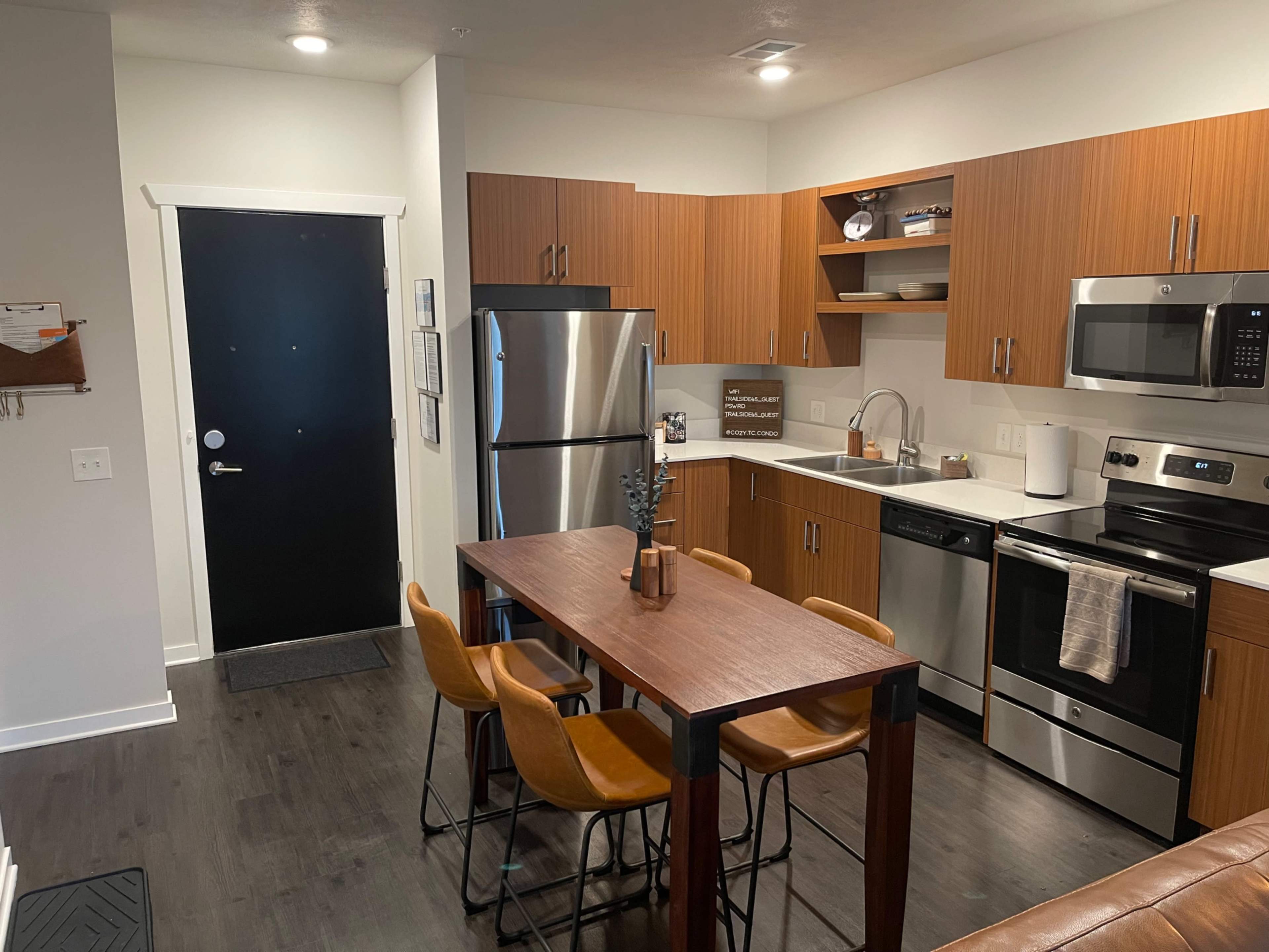 A modern kitchen and dining area featuring wooden cabinetry, stainless steel appliances, and a dining table with four chairs.