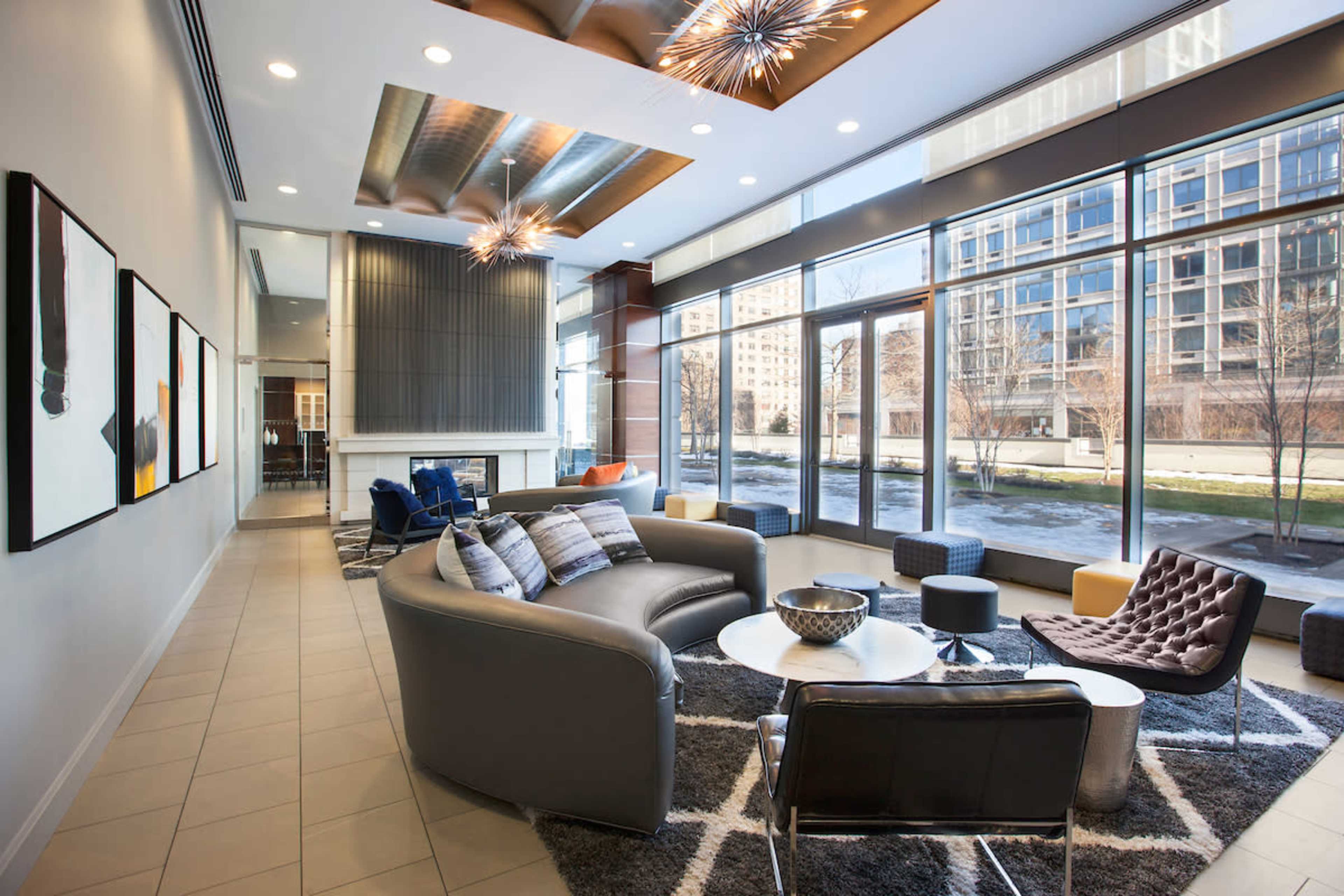 A modern lounge area with large windows, contemporary furniture, and decorative ceiling lights.