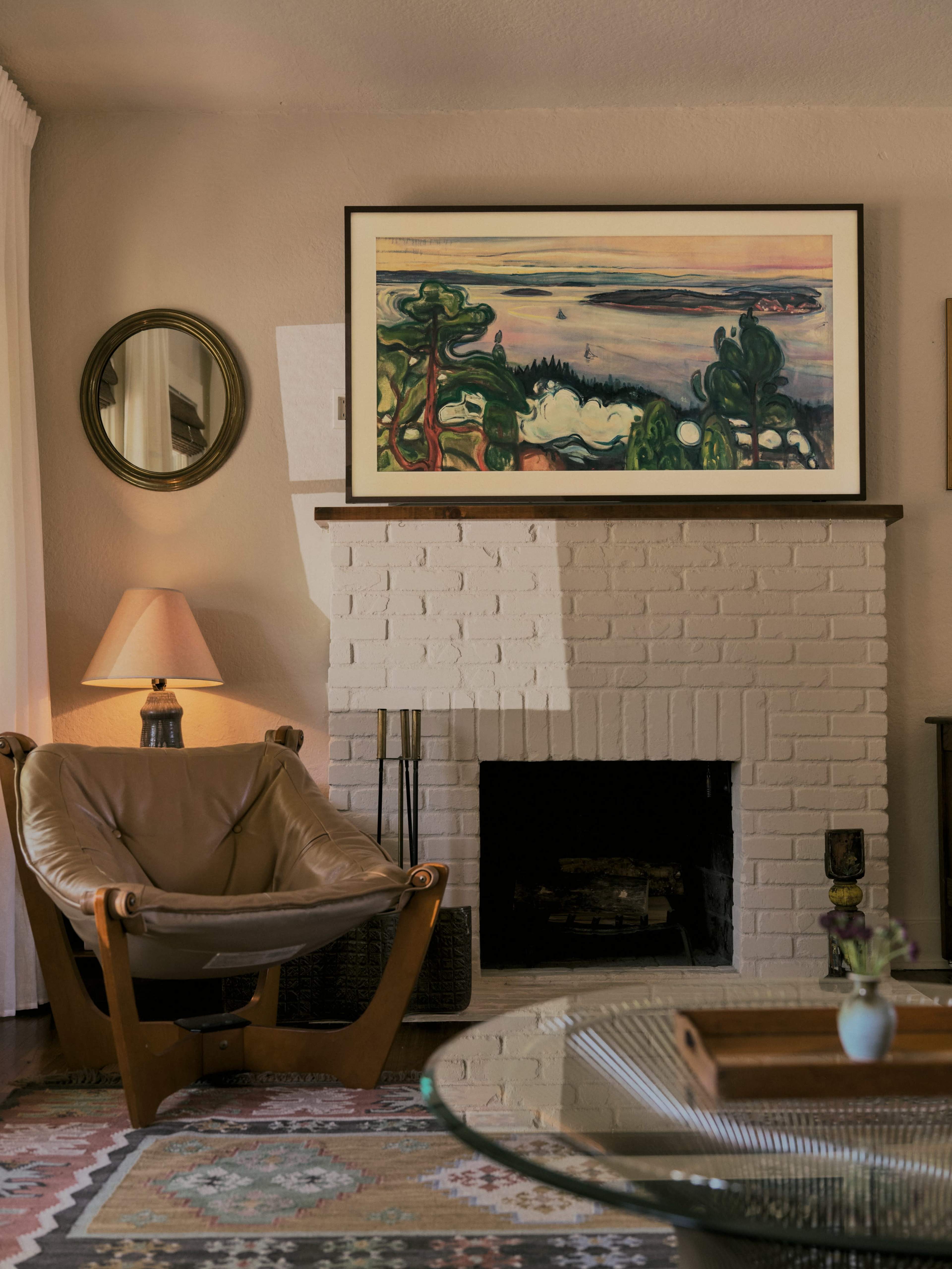 A cozy living room features a leather chair, a fireplace with a painting above it, and a decorative mirror on the wall.