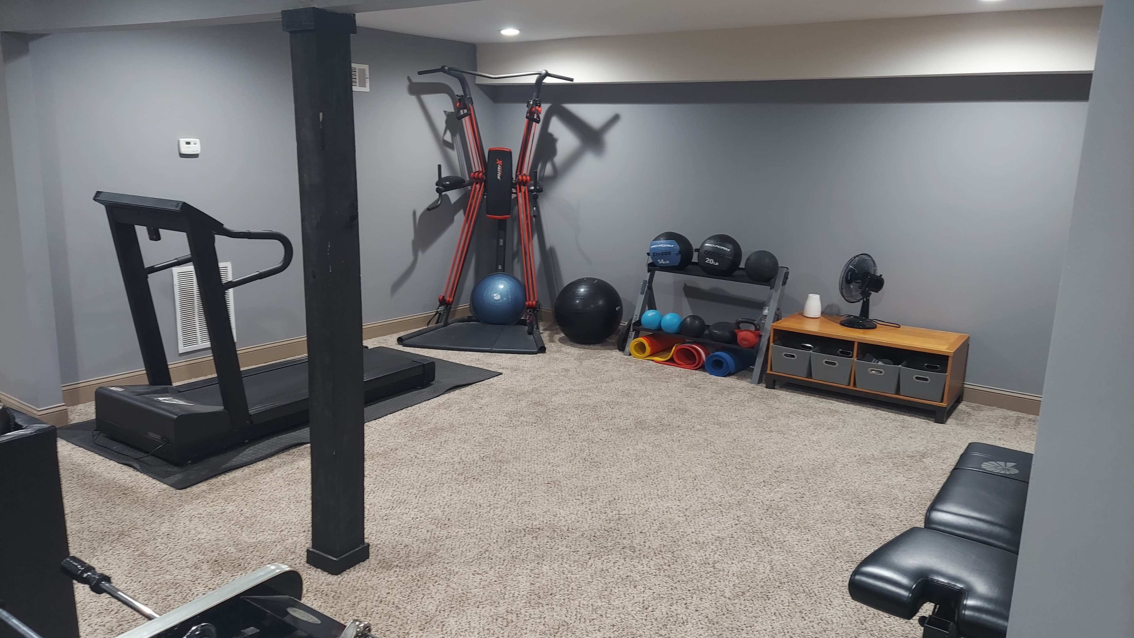 A home gym with various exercise equipment including a treadmill, weights, and a stability ball on a carpeted floor.