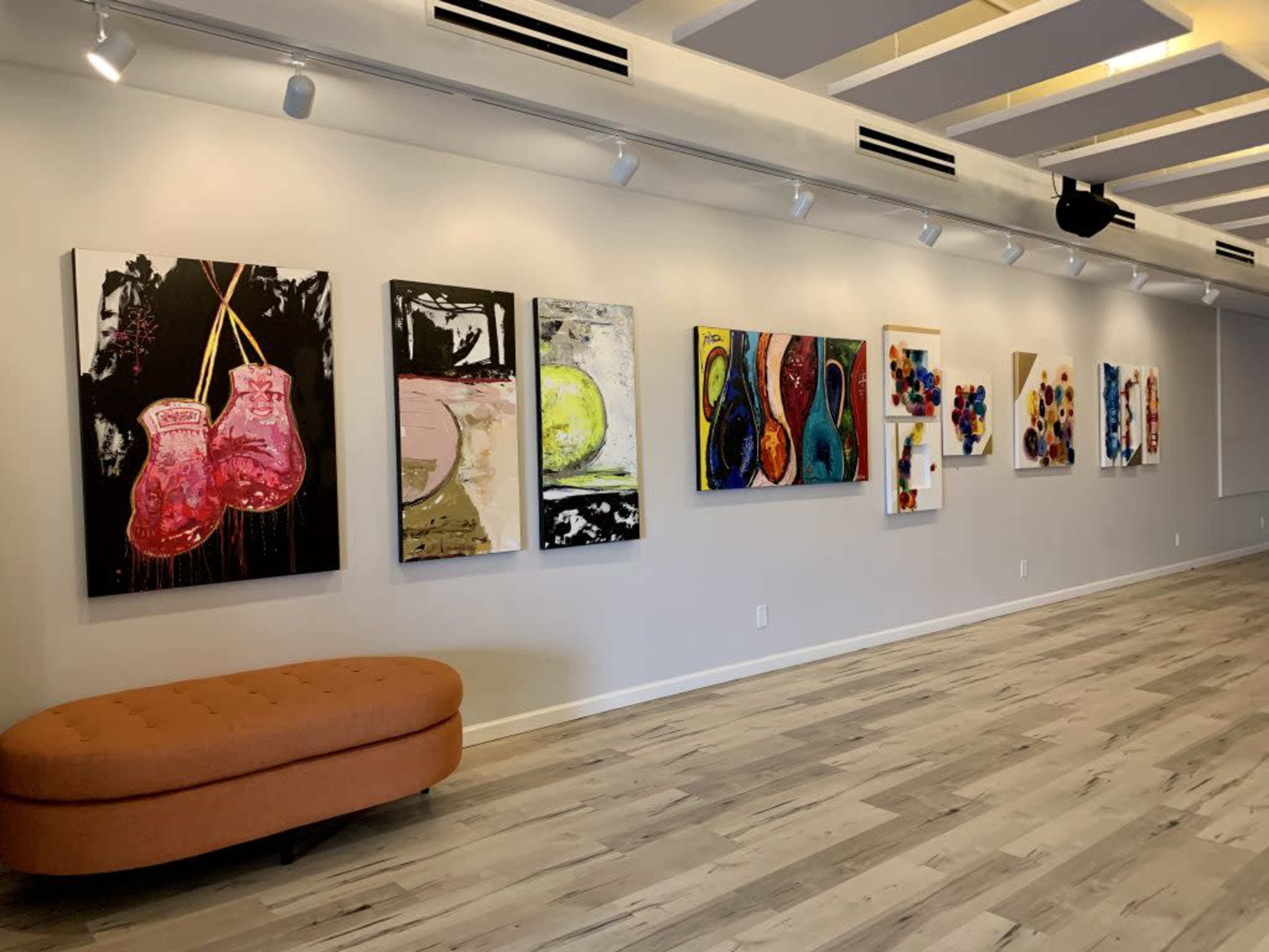 A gallery wall displaying a series of colorful abstract paintings, with an orange curved sofa positioned nearby.