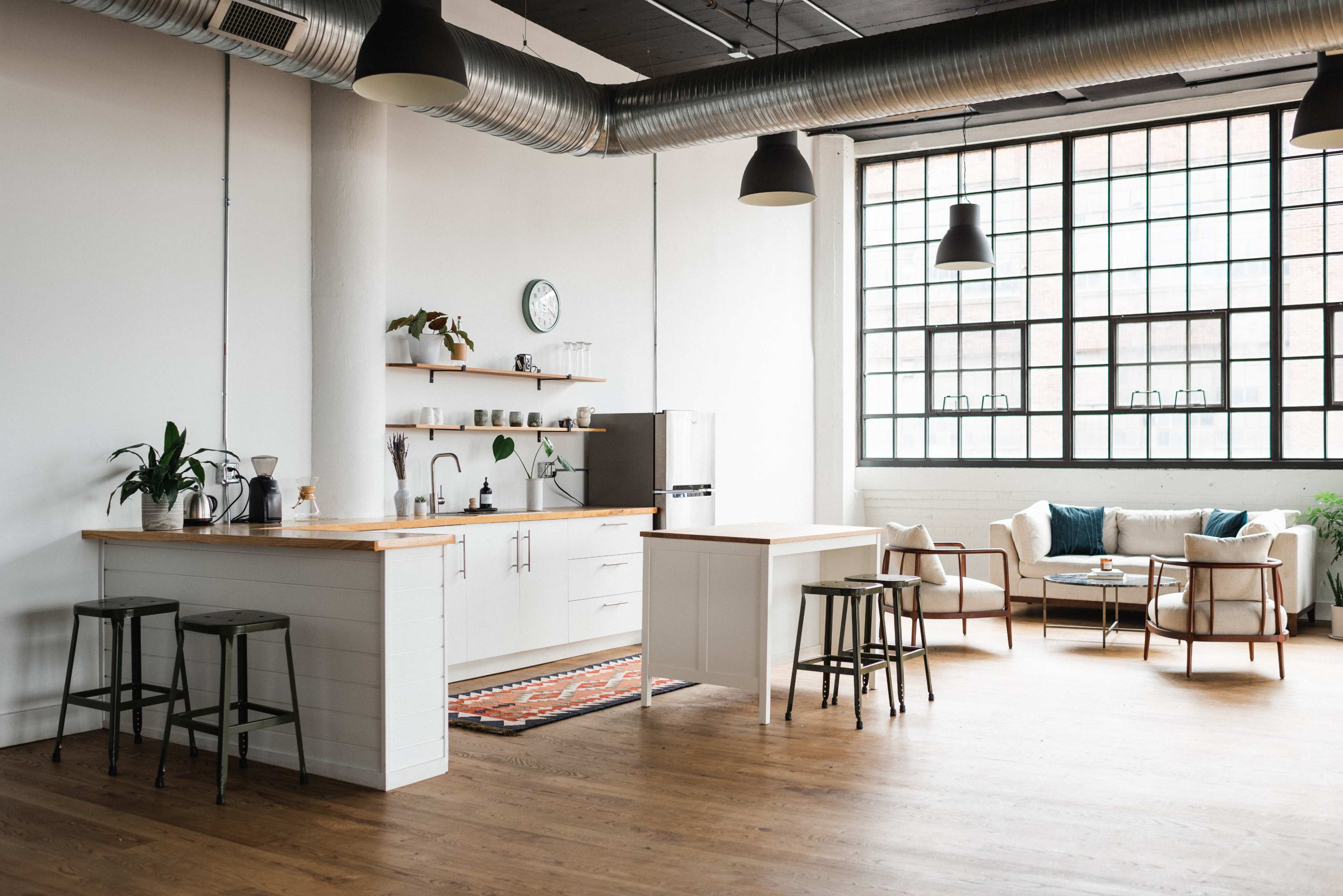 A modern kitchen and living area with wooden floors, a large window, and minimalist furnishings.
