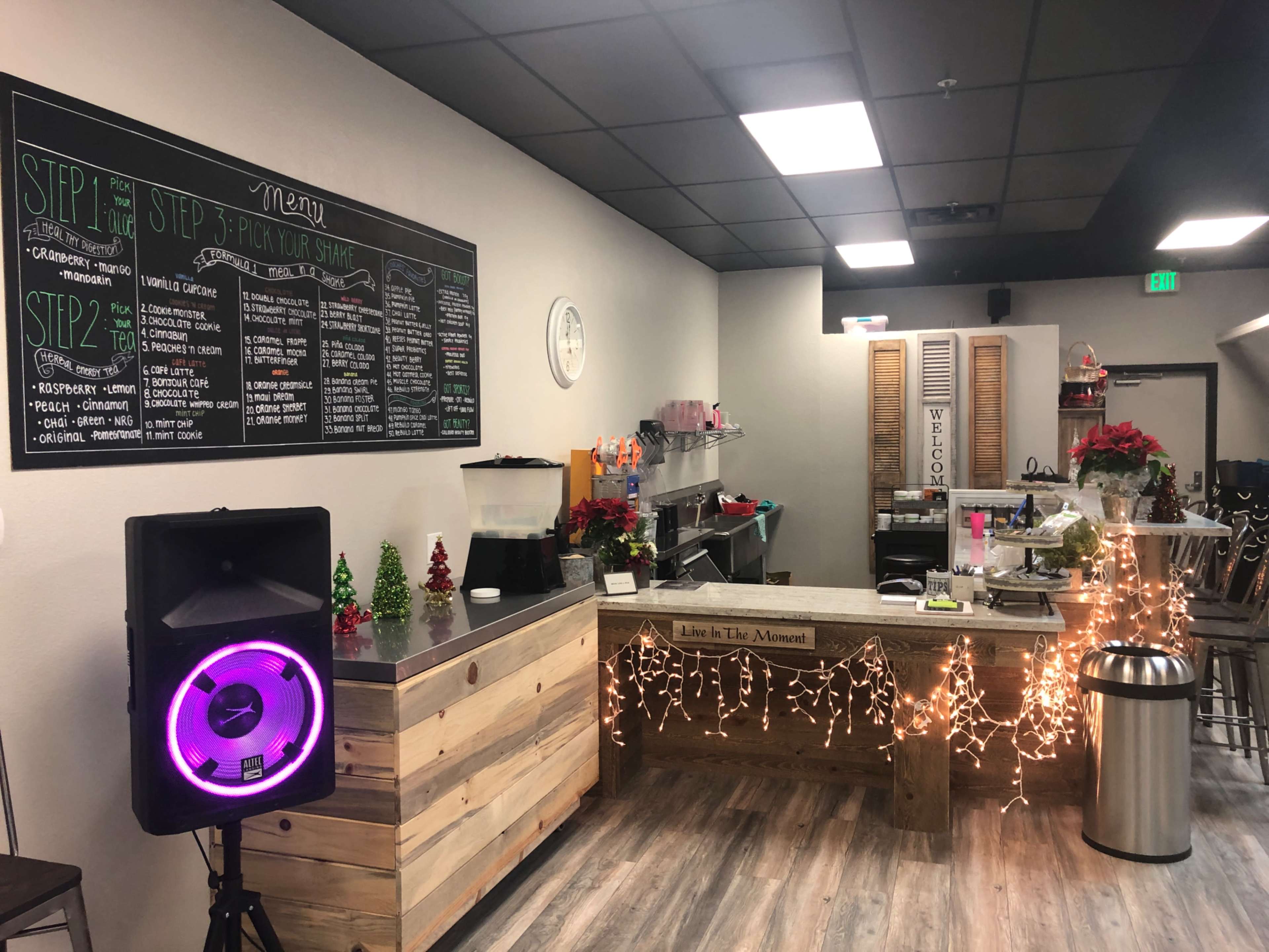 A coffee shop interior with a service counter decorated with lights and holiday-themed items, and a large chalkboard menu on the wall.