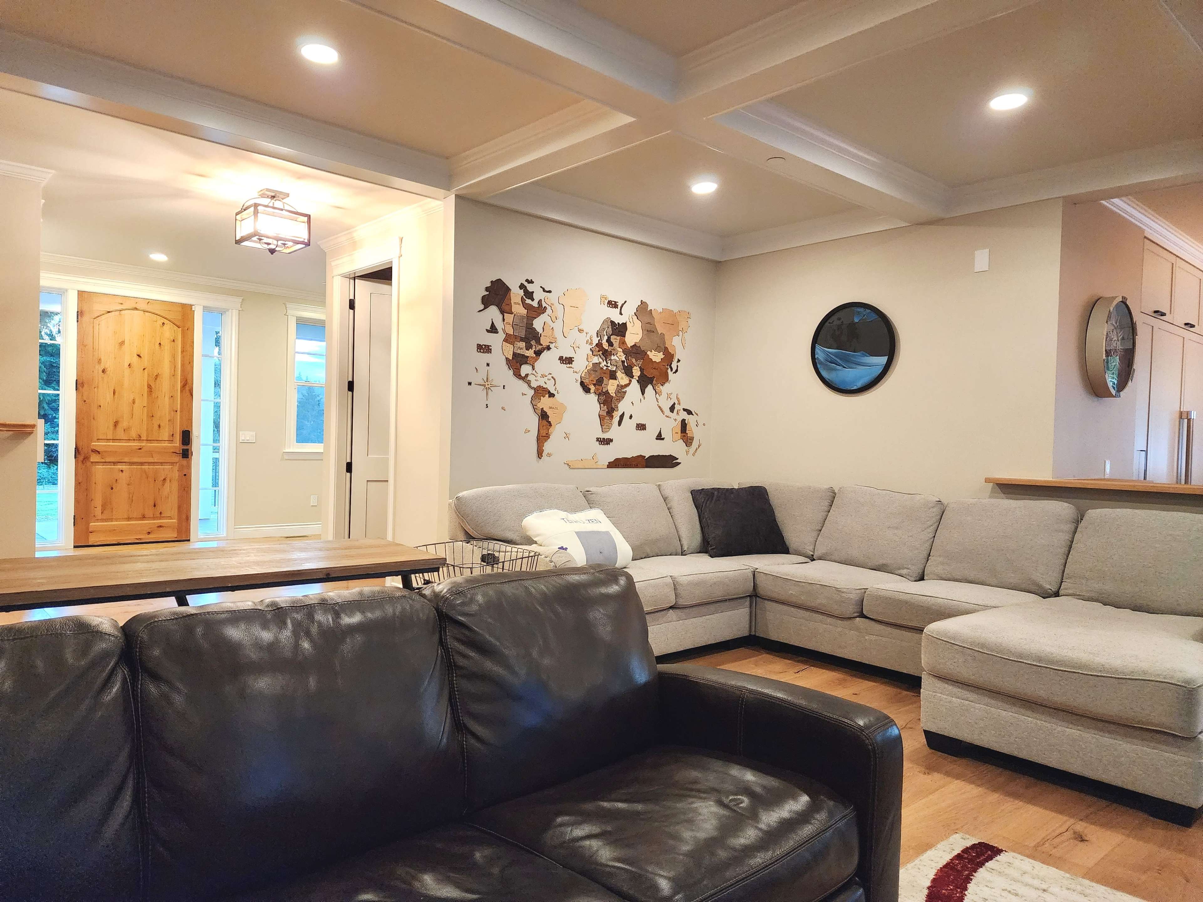 A spacious living room features a sectional sofa, a wooden coffee table, and a world map art piece on the wall, with a door leading outside visible in the background.