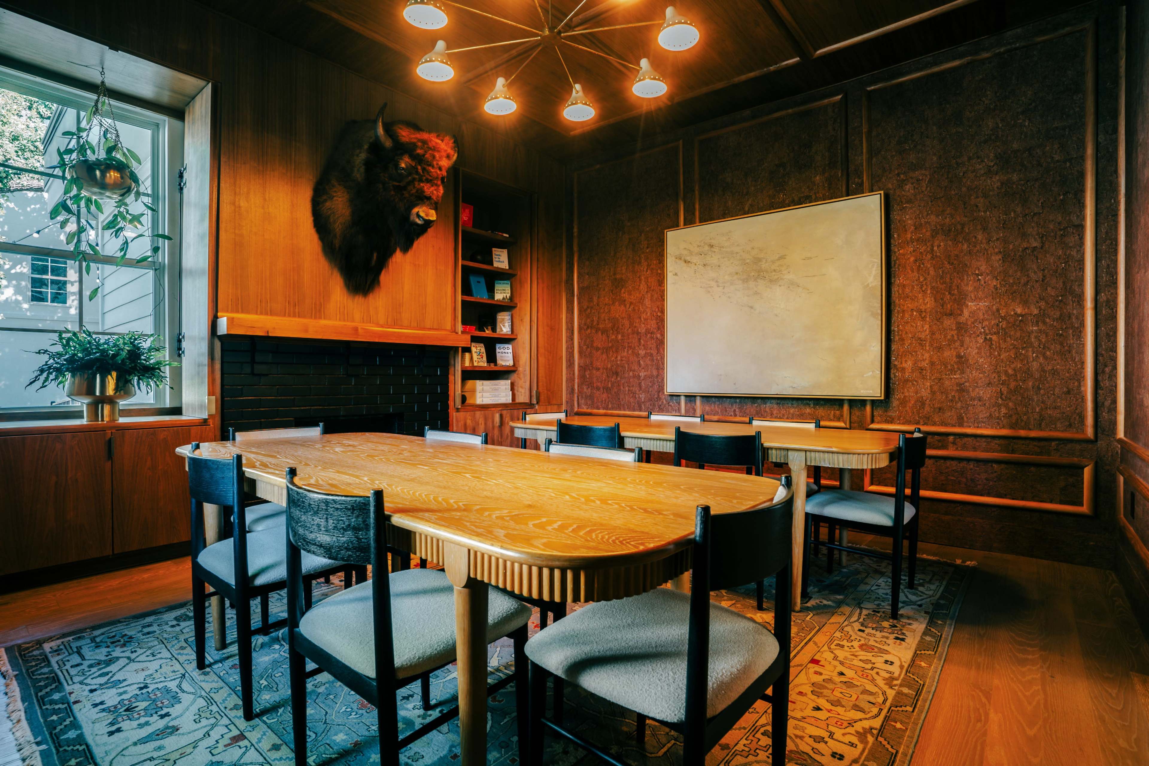 The image shows a wood-paneled conference room featuring a long wooden table with chairs, a mounted buffalo head on the wall, and a large, blank whiteboard.